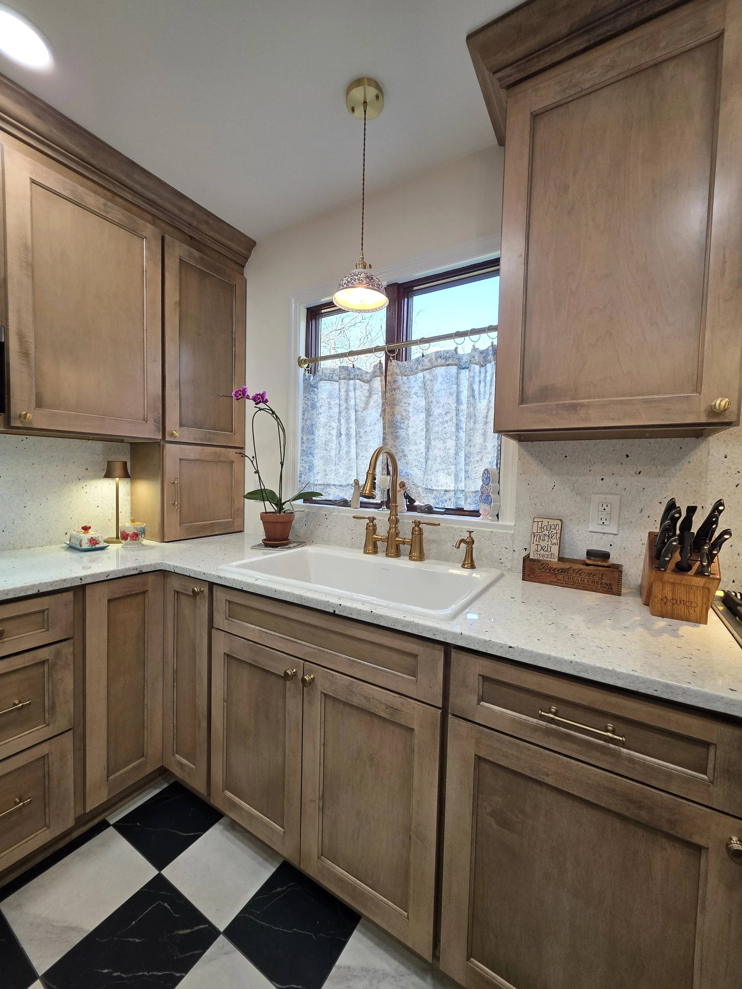 White farmhouse sink with gold-tone faucet beneath pendant lighting.