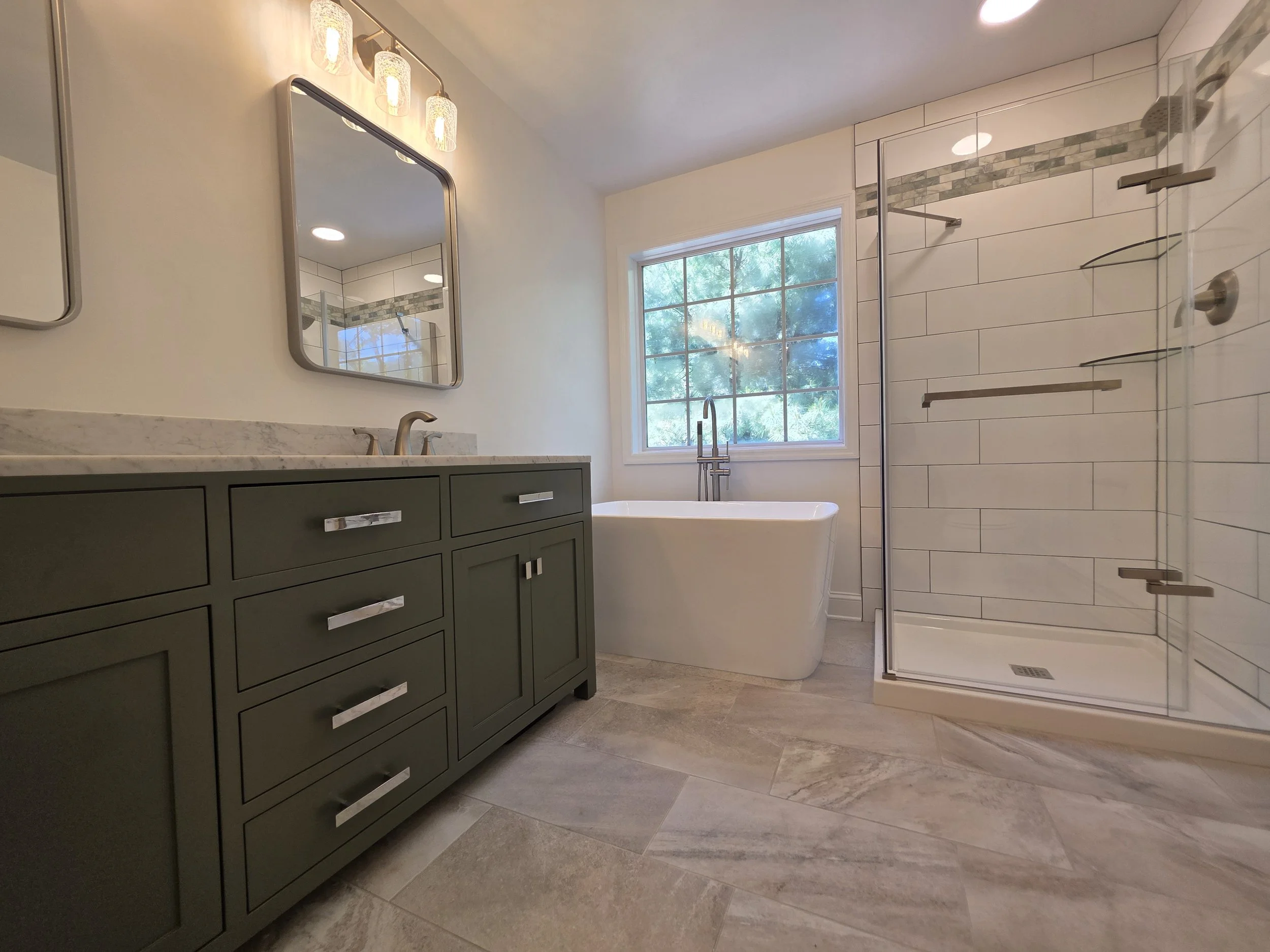 Low view of the green vanity cabinetry, patterned floor and freestanding bathtub.