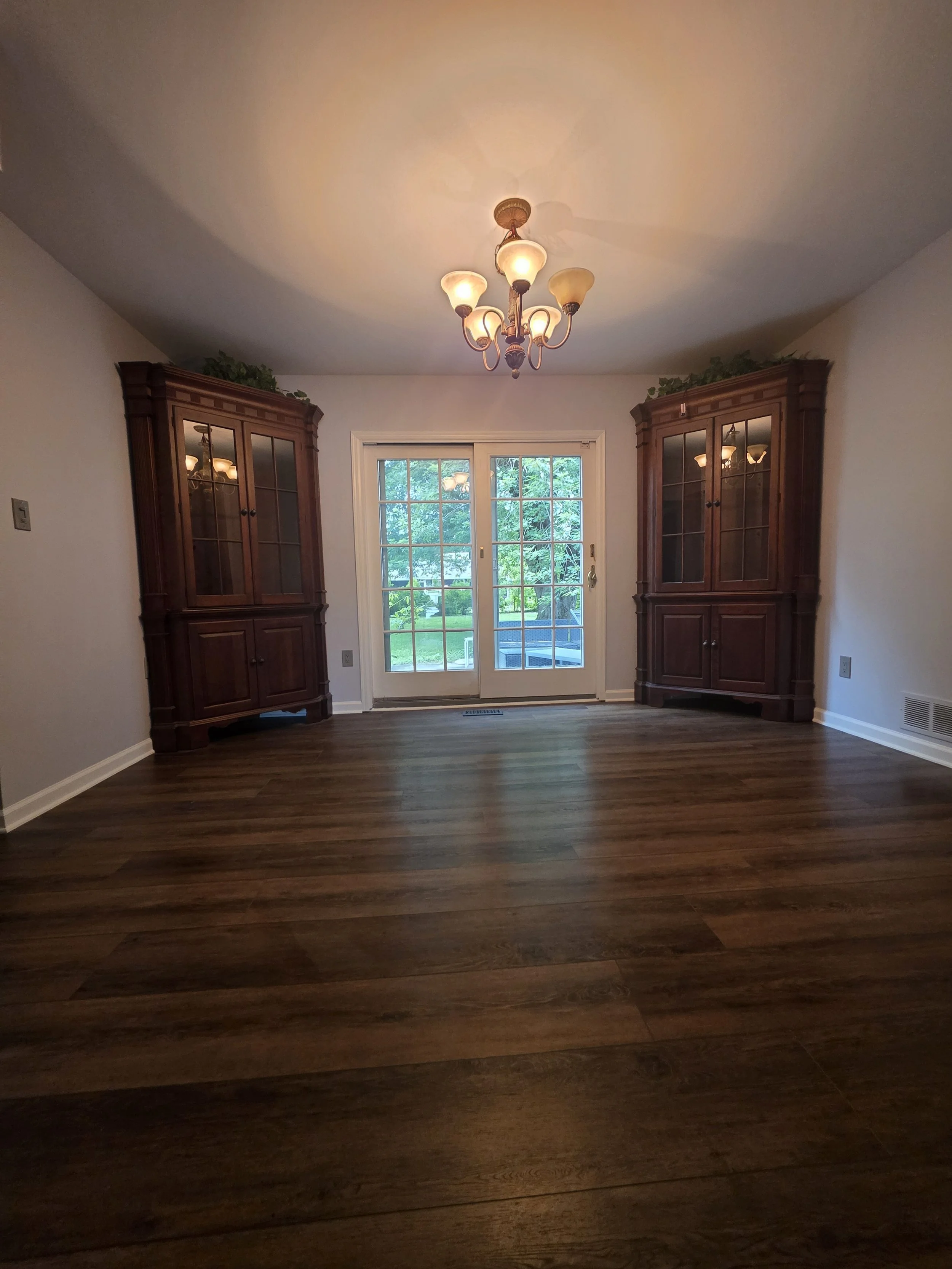 Tim and Mary’s refreshed dining room with dark wood-look flooring, pale walls and corner display cabinets.