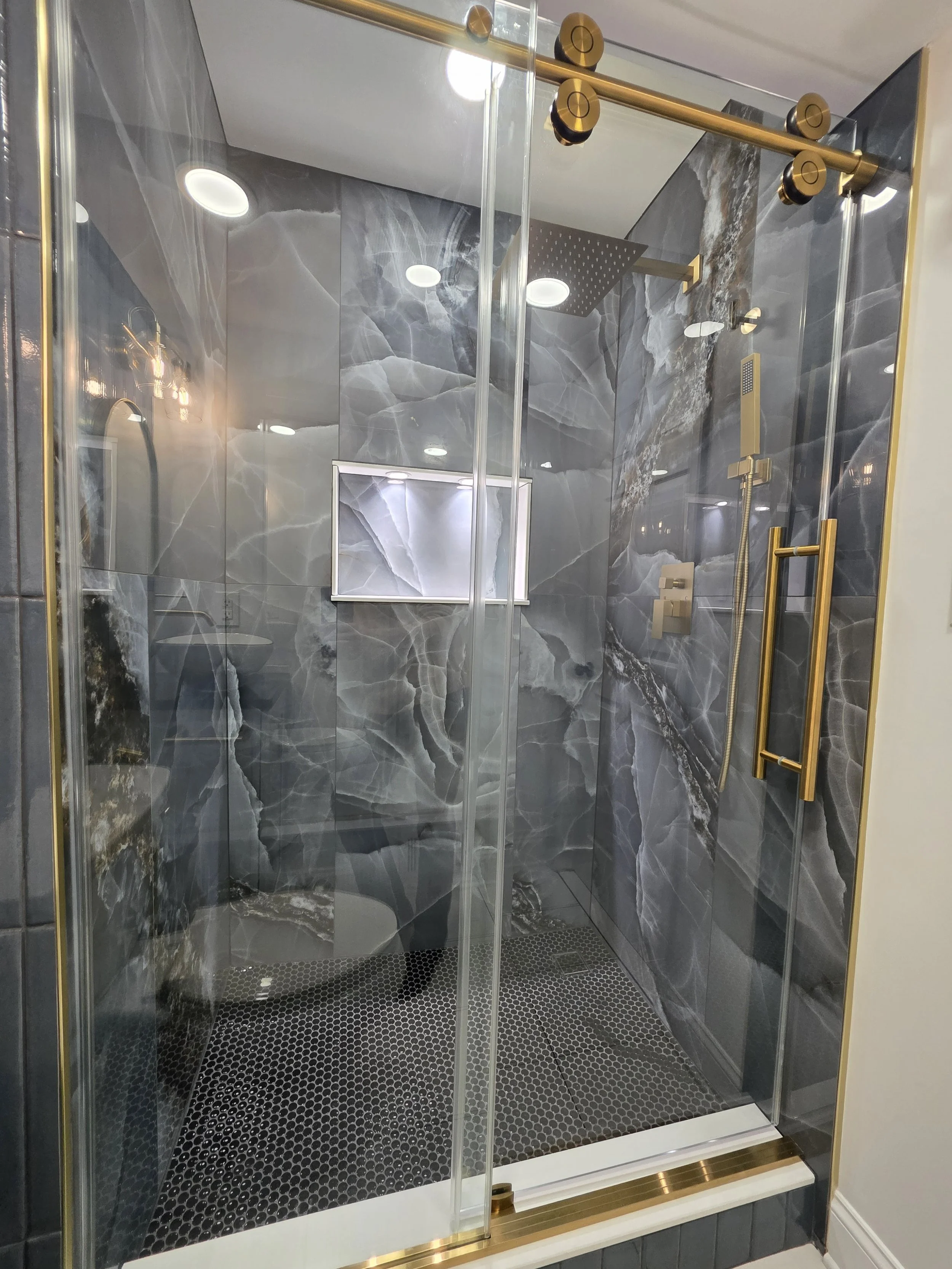 Glass shower enclosure with gold-tone sliding hardware, veined wall tile and an illuminated recessed niche.