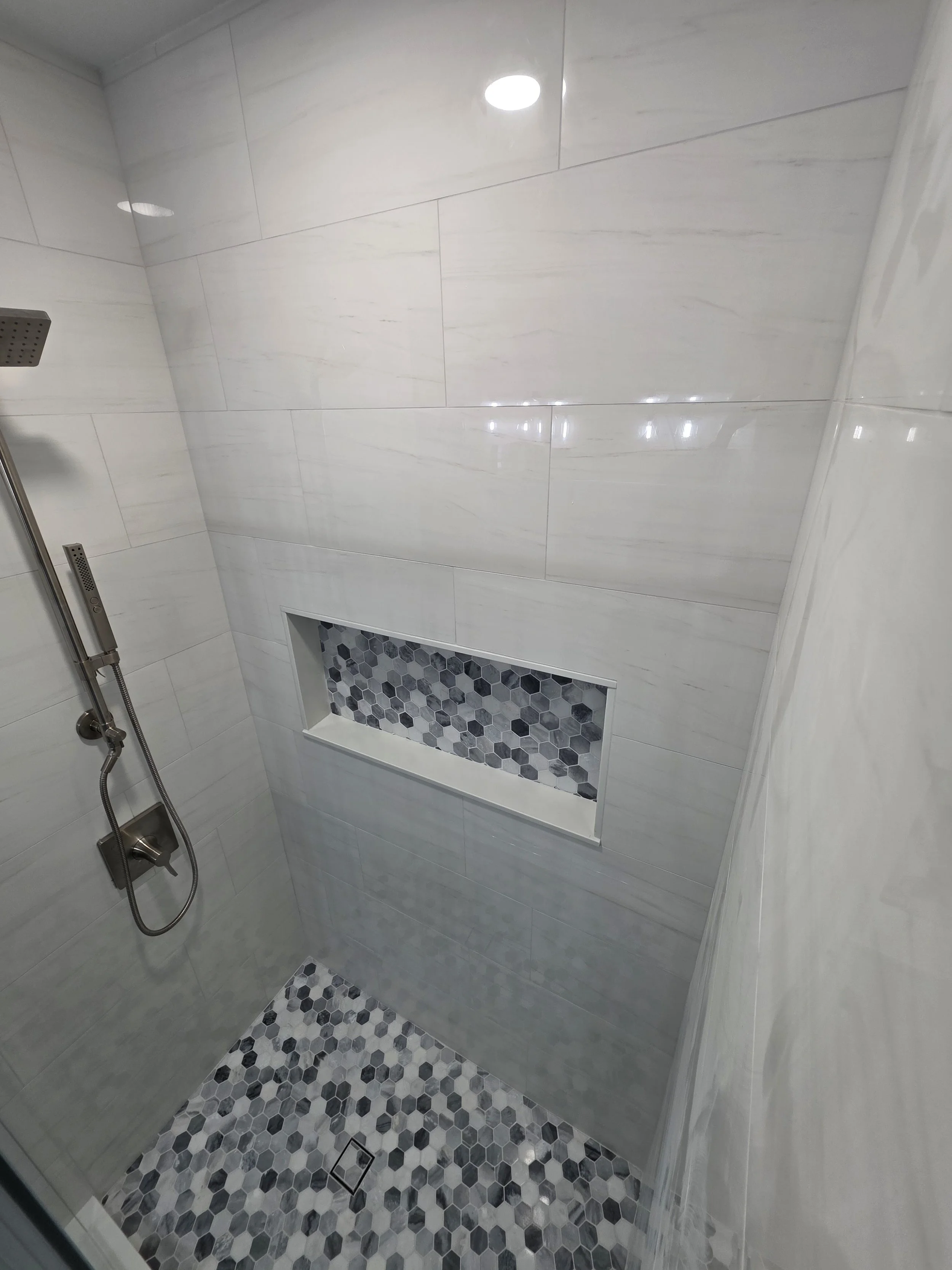 White shower wall tile and patterned shower floor.