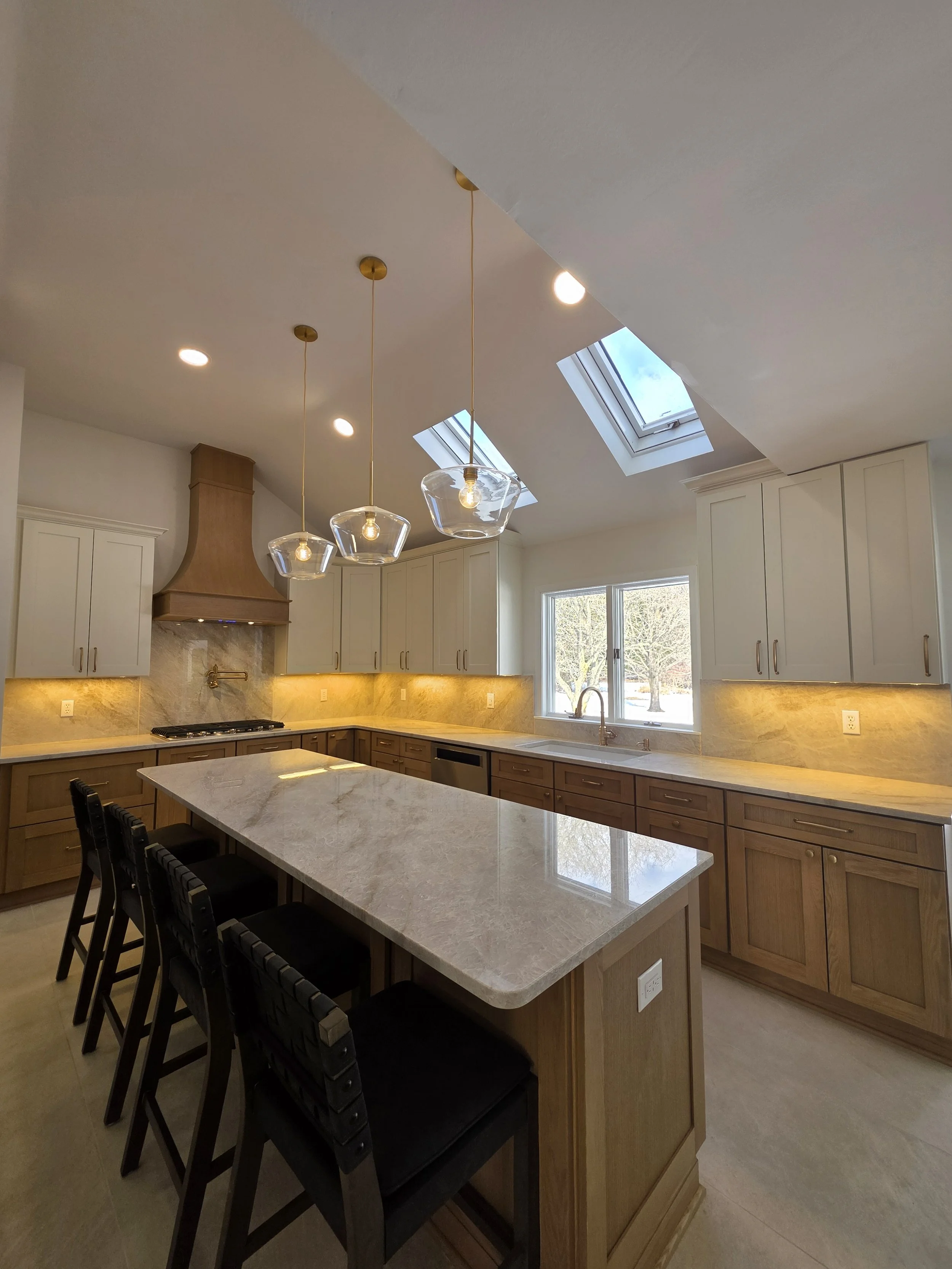 Island seating and veined countertop beneath glass pendant lights and skylights.