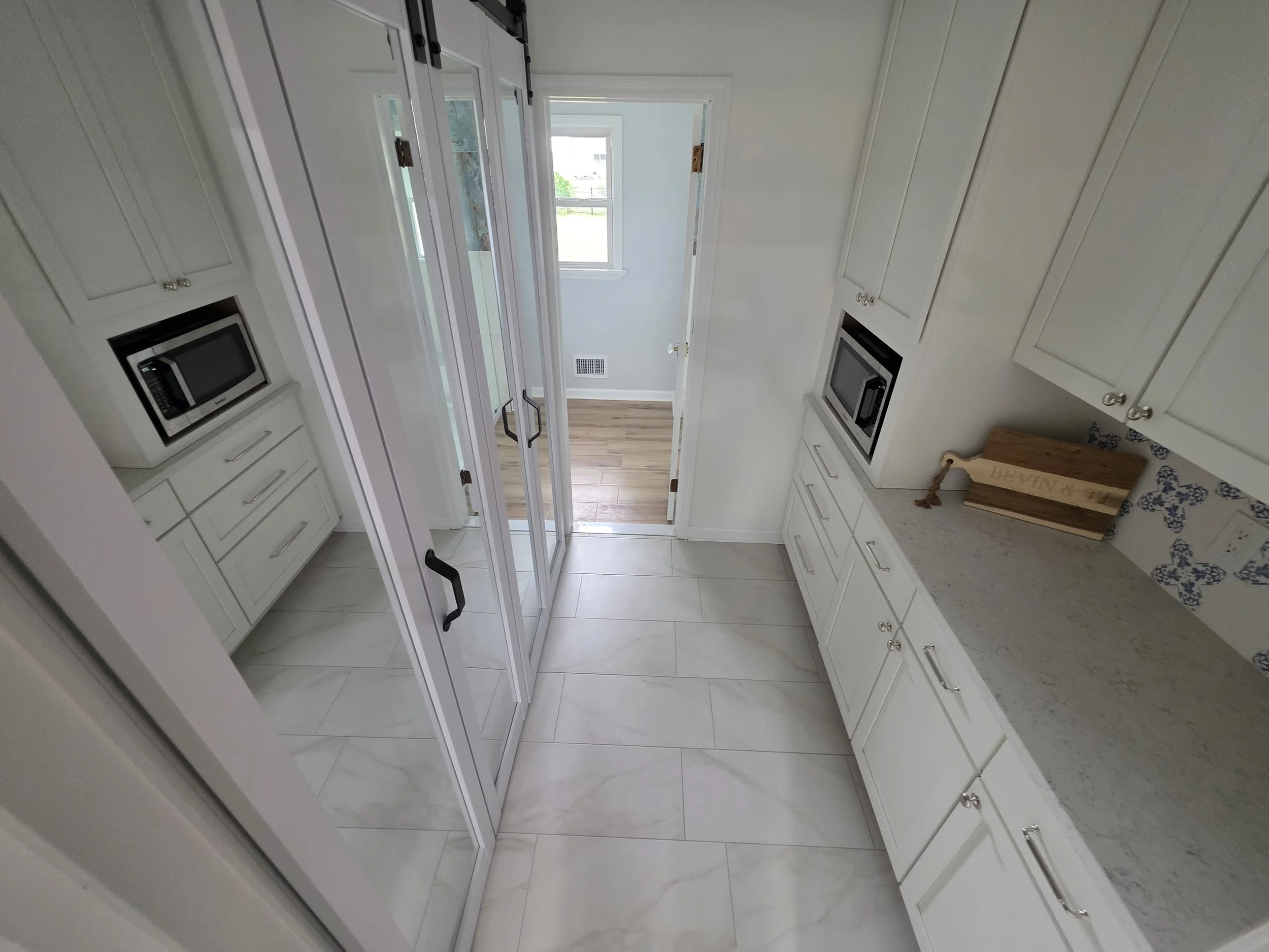 Laundry and pantry passage with white cabinets and mirrored doors.