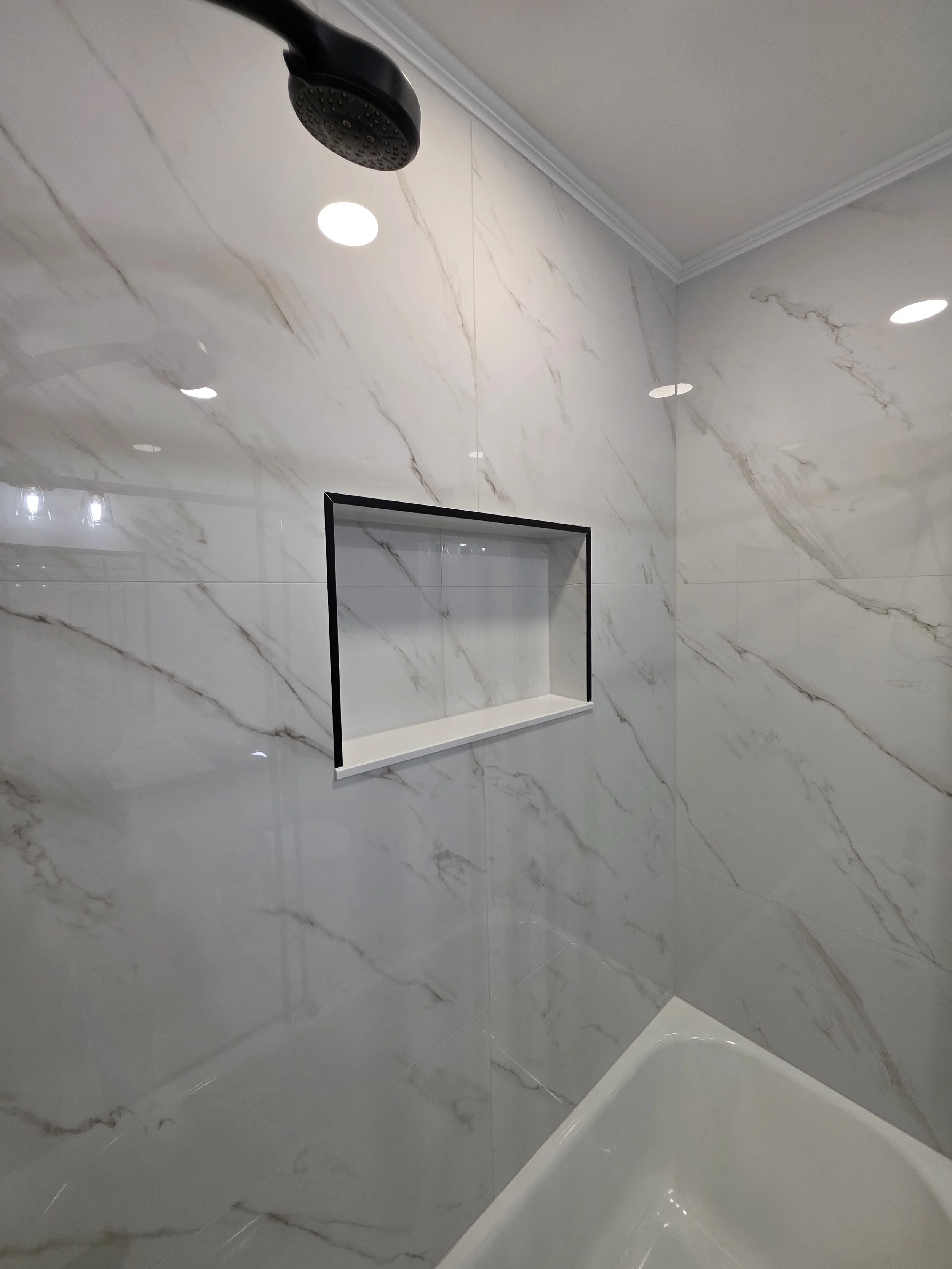 Close view of the tiled tub surround, black showerhead and recessed niche.