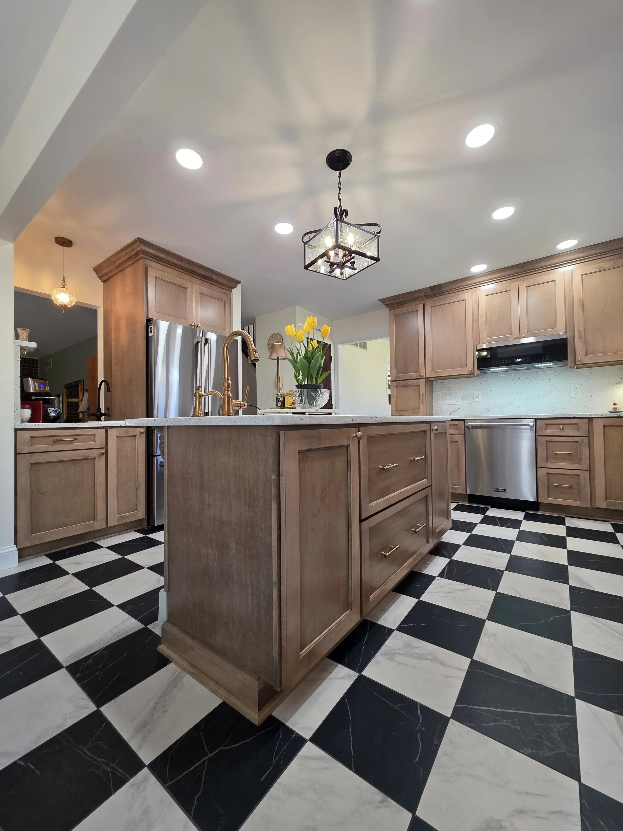 Island and wood cabinetry beneath decorative lighting, with stainless appliances behind.