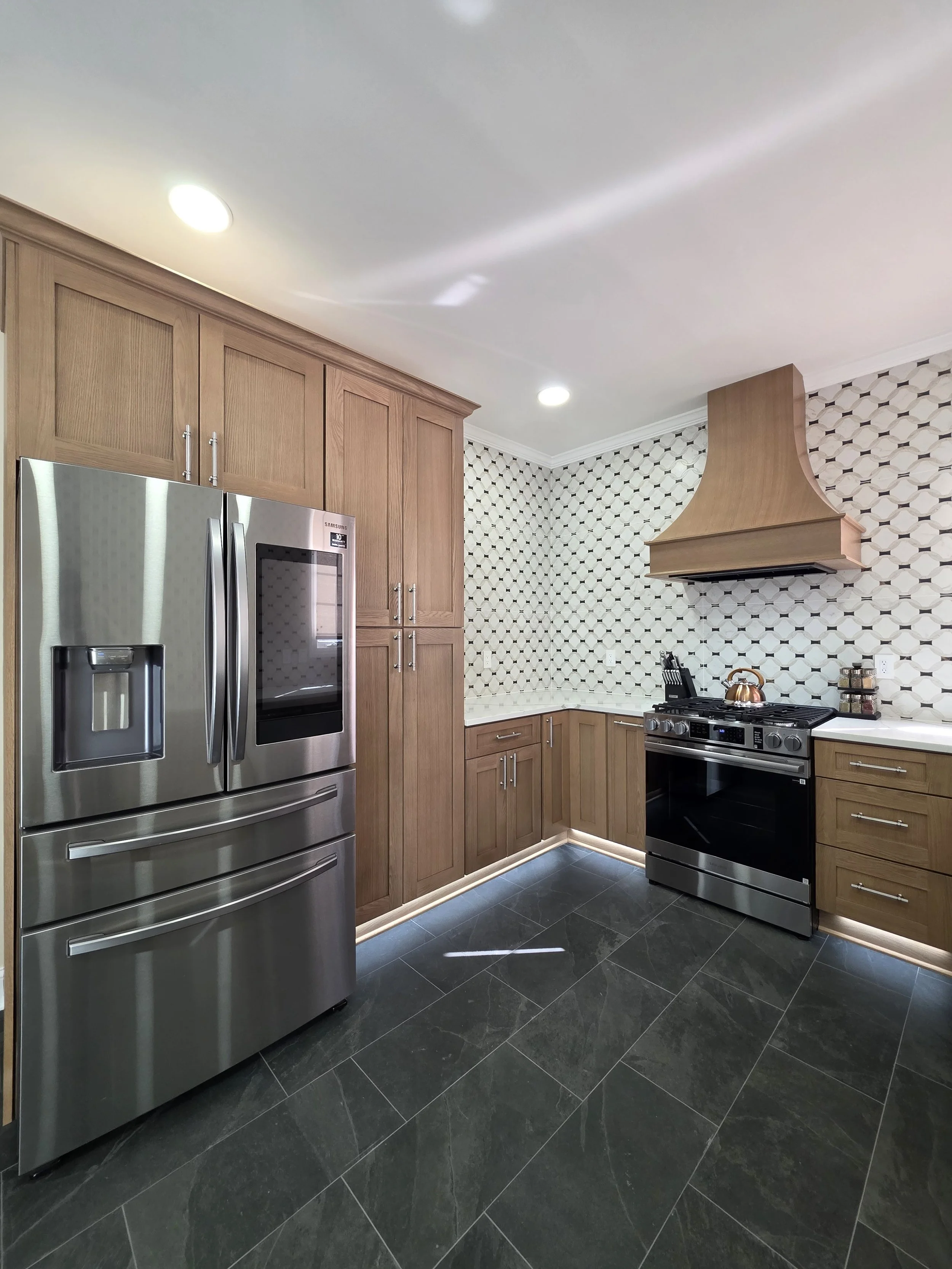 Wood range hood and cabinetry beside stainless refrigerator.