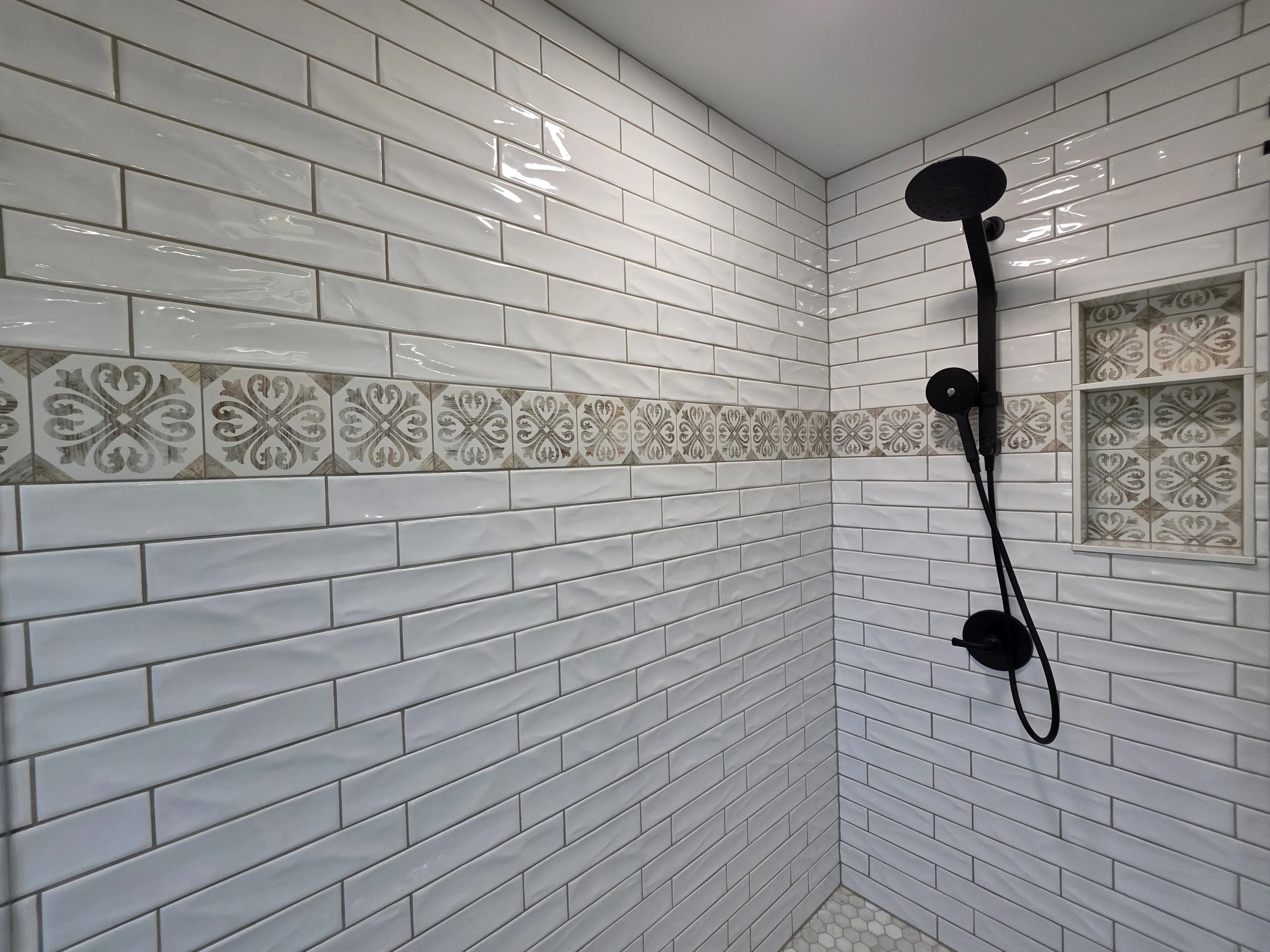 White subway-tile shower wall with a decorative tile band and black shower fixtures.