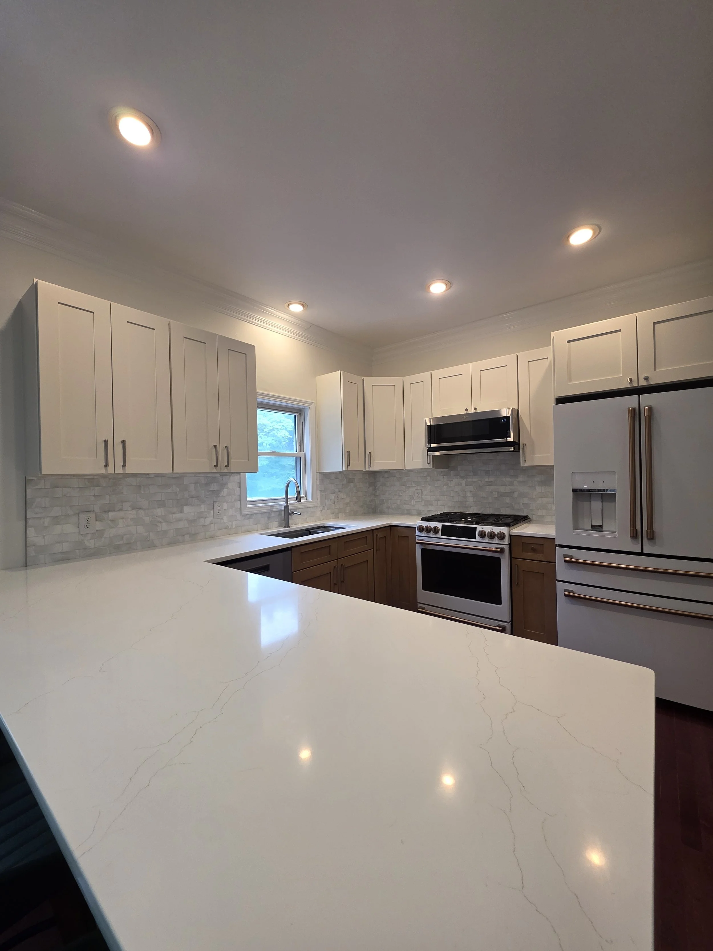 Wide view across the light kitchen countertop toward white upper cabinets and the retained flooring.