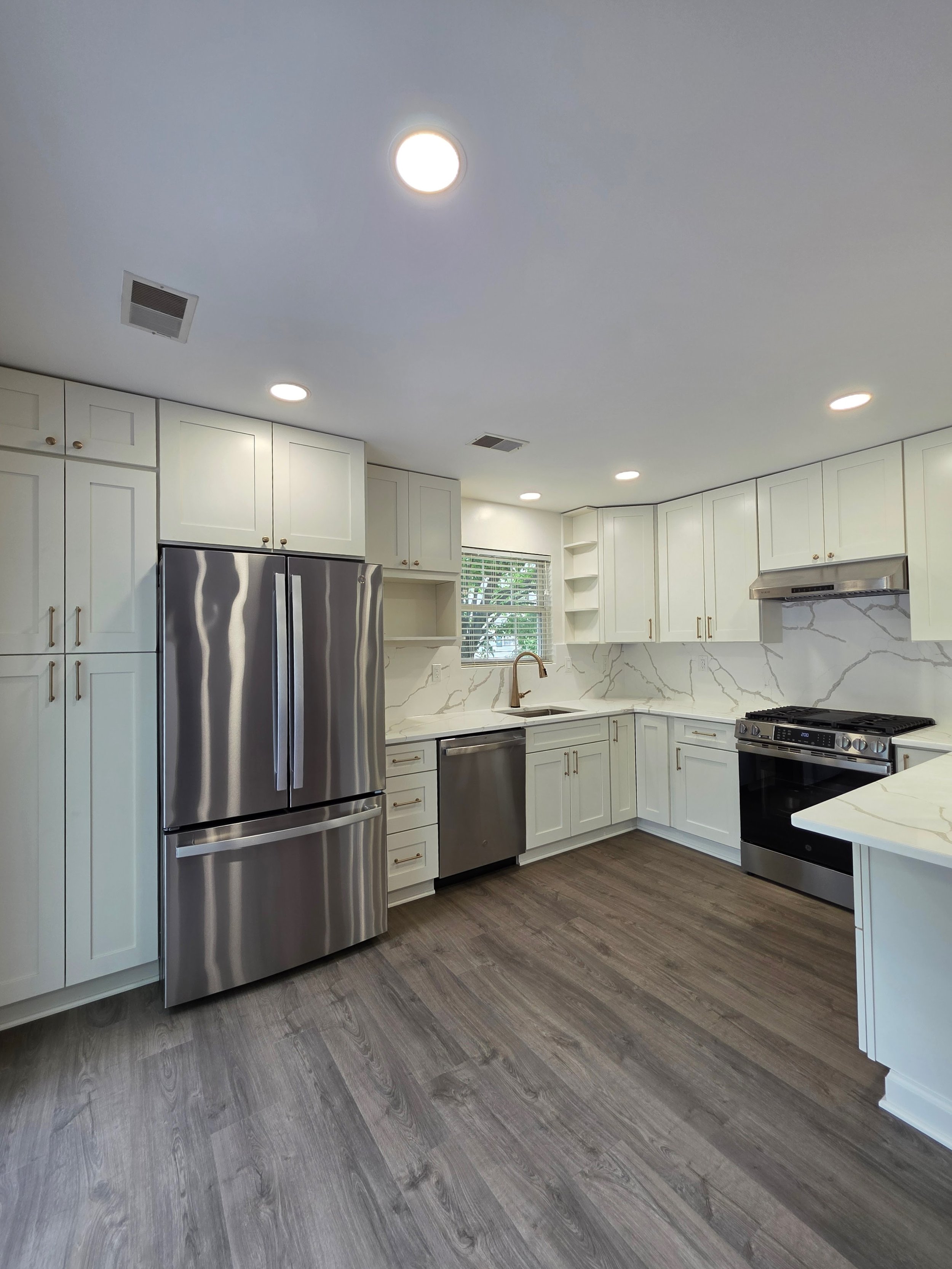 White cabinetry, stainless refrigerator and sink beneath the window in the finished kitchen.