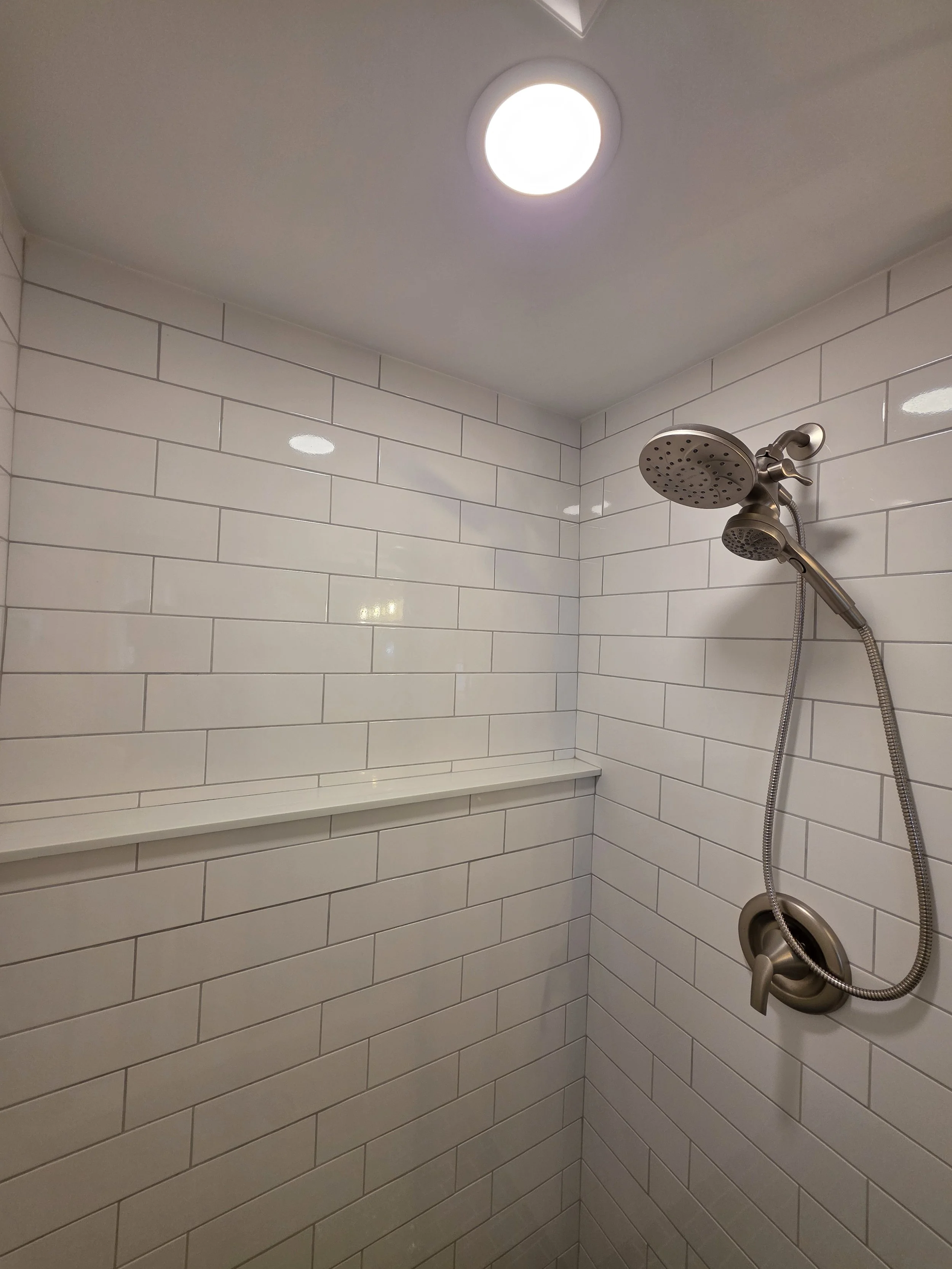 Handheld shower and controls against white subway tile with a long tiled ledge.