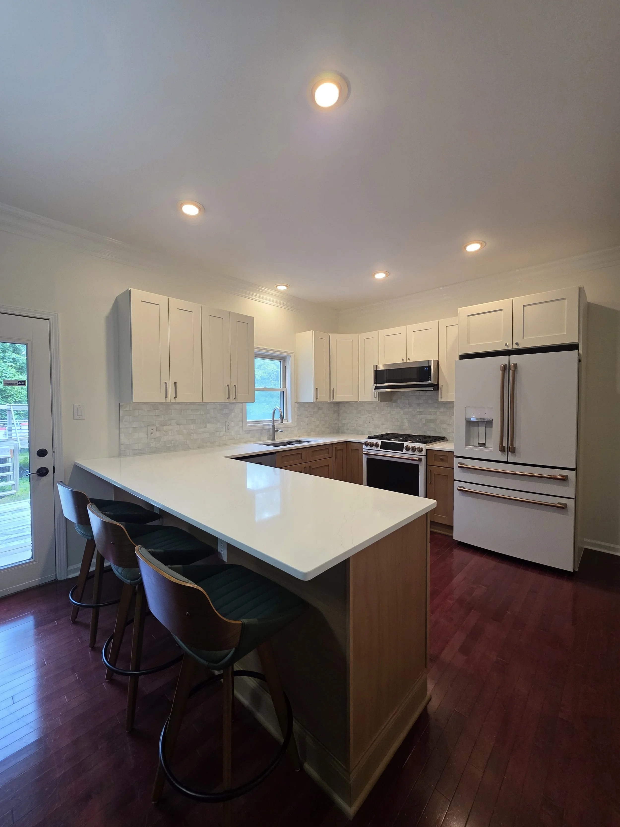 Updated kitchen with white upper cabinets, wood-tone lower cabinets, light countertops, and peninsula seating.