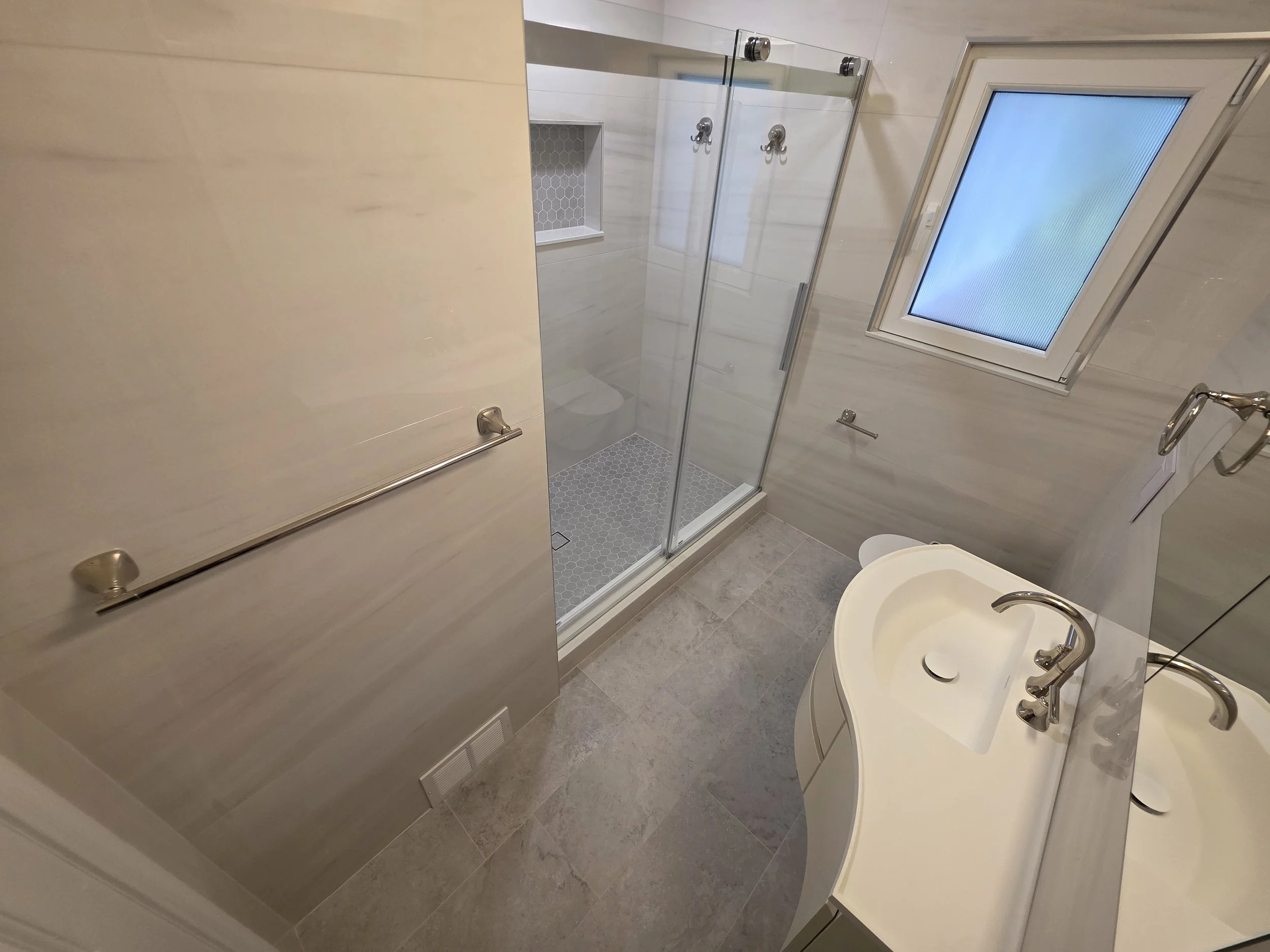Glass shower enclosure and curved vanity seen from doorway.