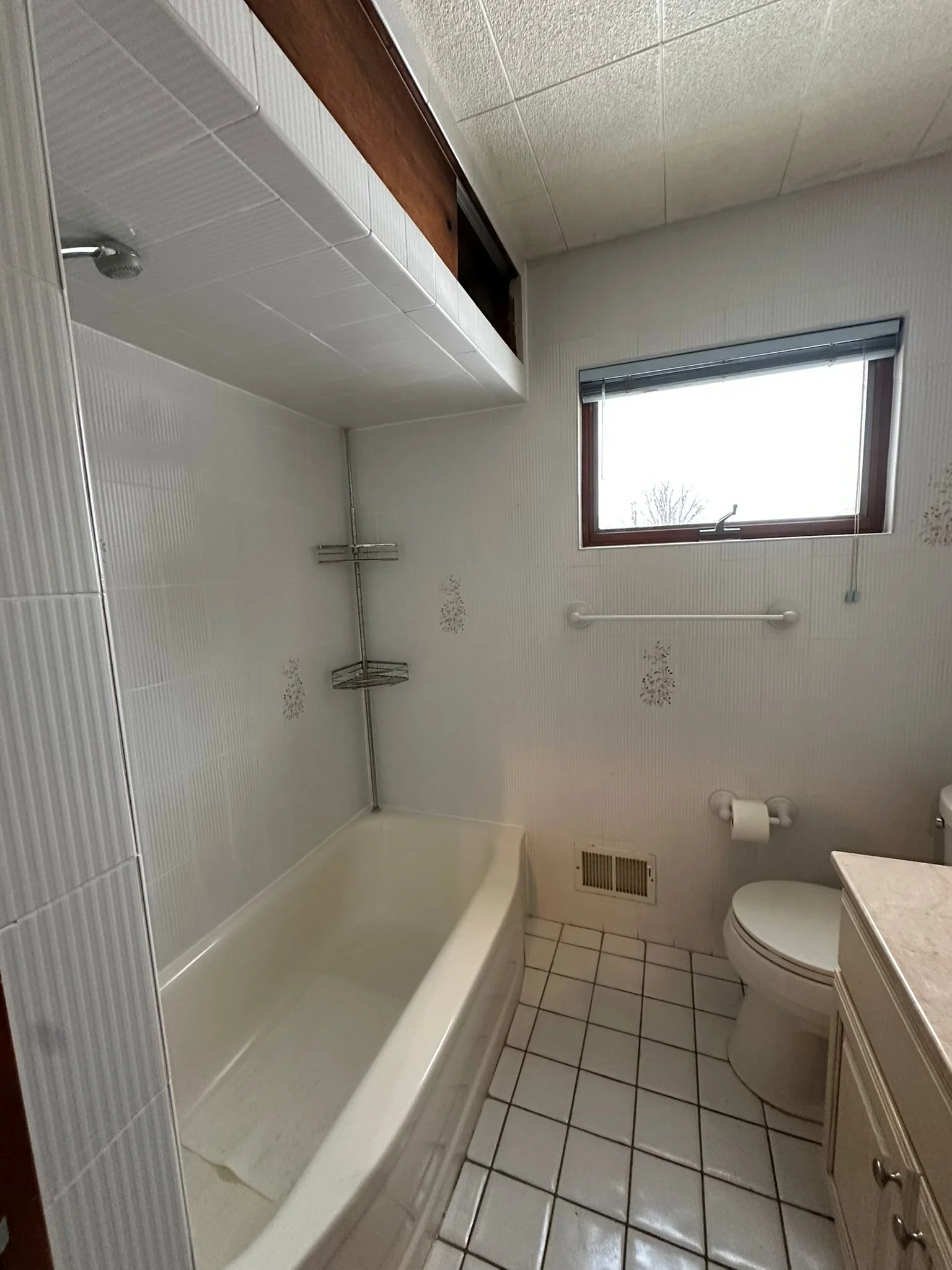 Before renovation: the original bathtub, older tile floor and walls, toilet and window in Samuel’s hallway bathroom.