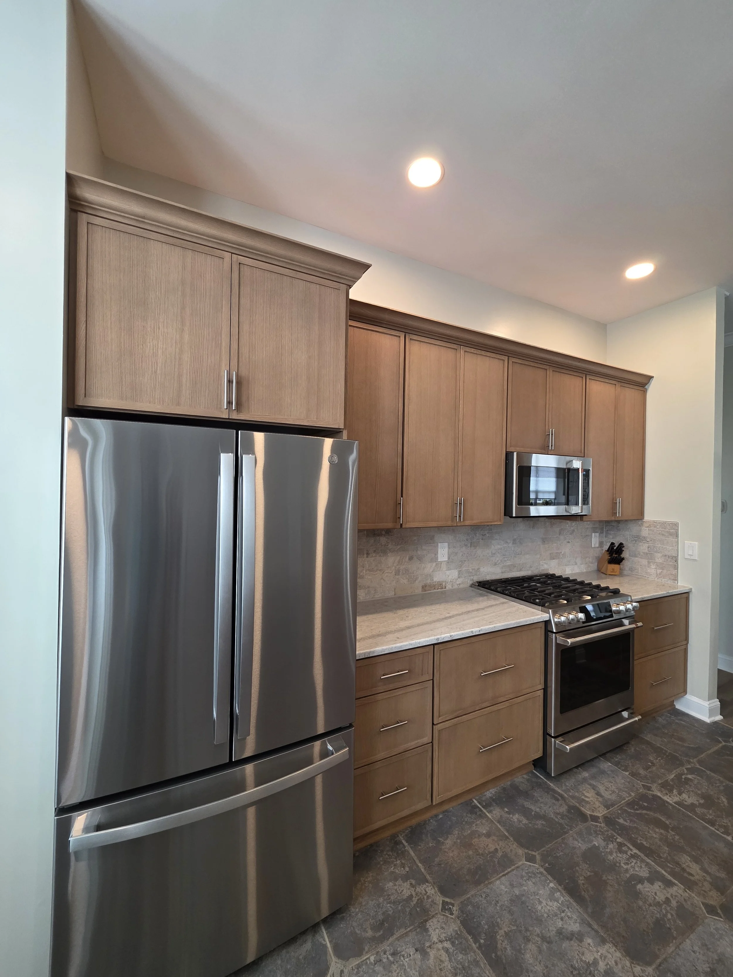 Stainless refrigerator and range beneath wood cabinets with continuous crown molding.