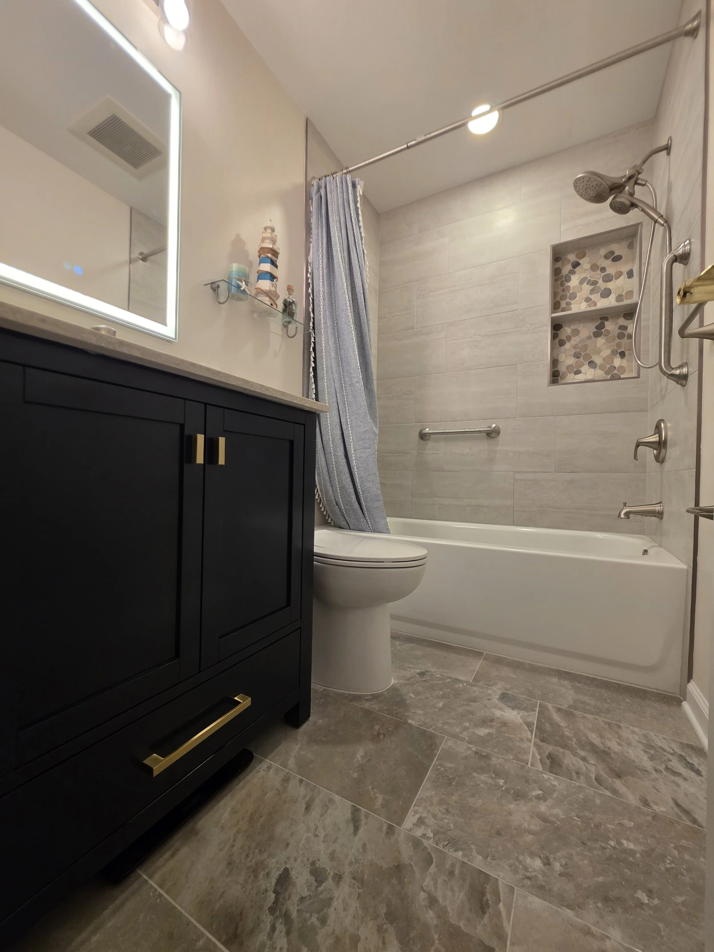 Low view of the navy vanity, toilet, light patterned floor and white bathtub.