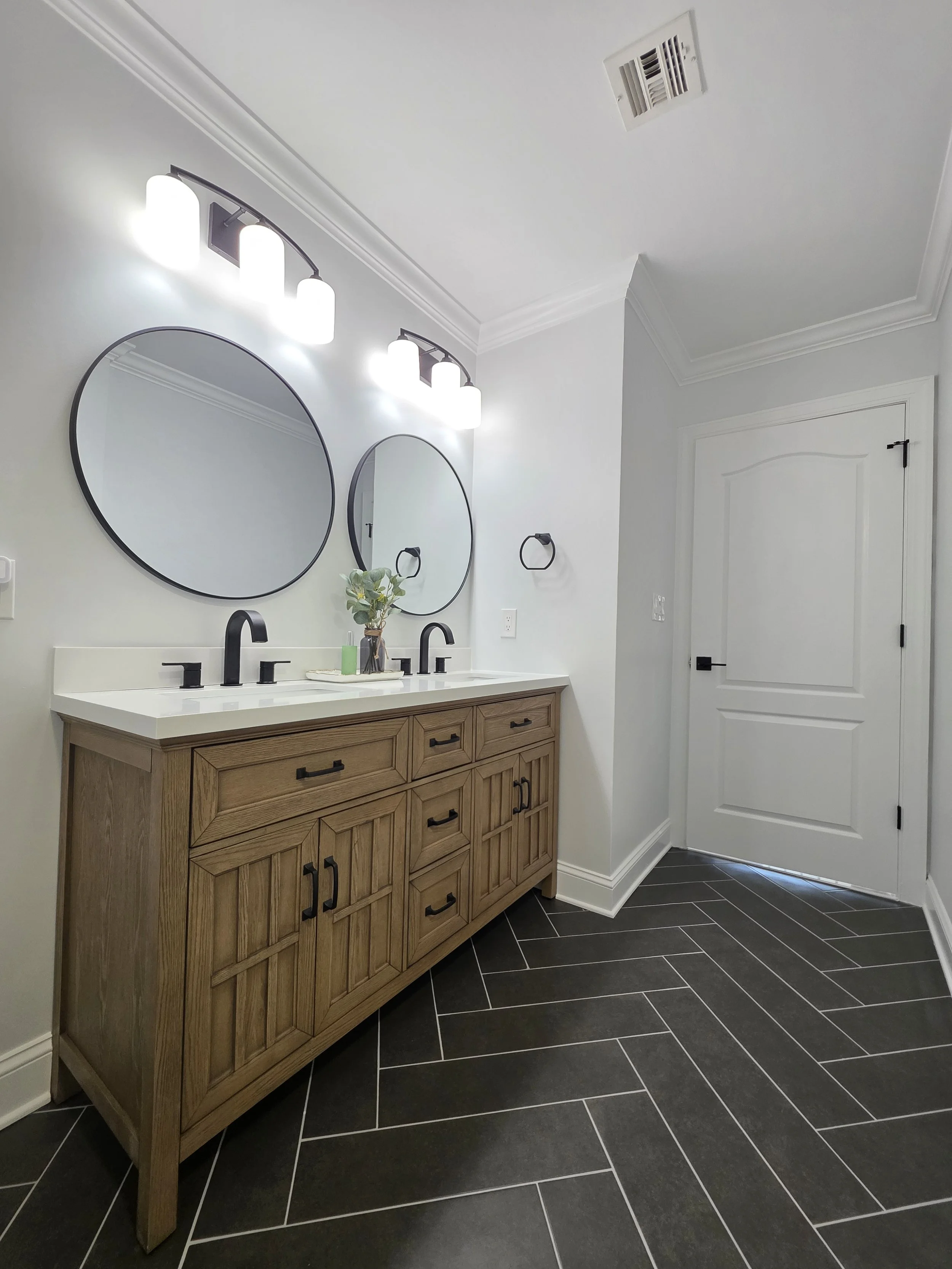 Double vanity with black faucets, round mirrors and overhead lighting in Alan and Alissa’s remodeled hallway bathroom.