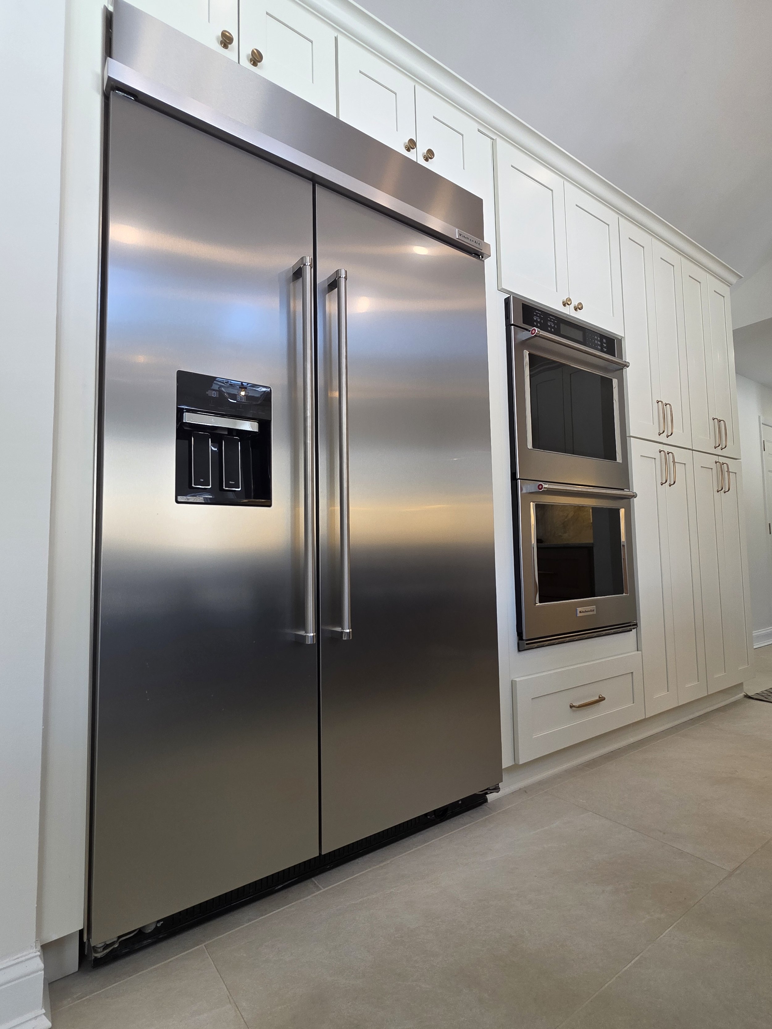 Stainless refrigerator and built-in ovens framed by white cabinetry.