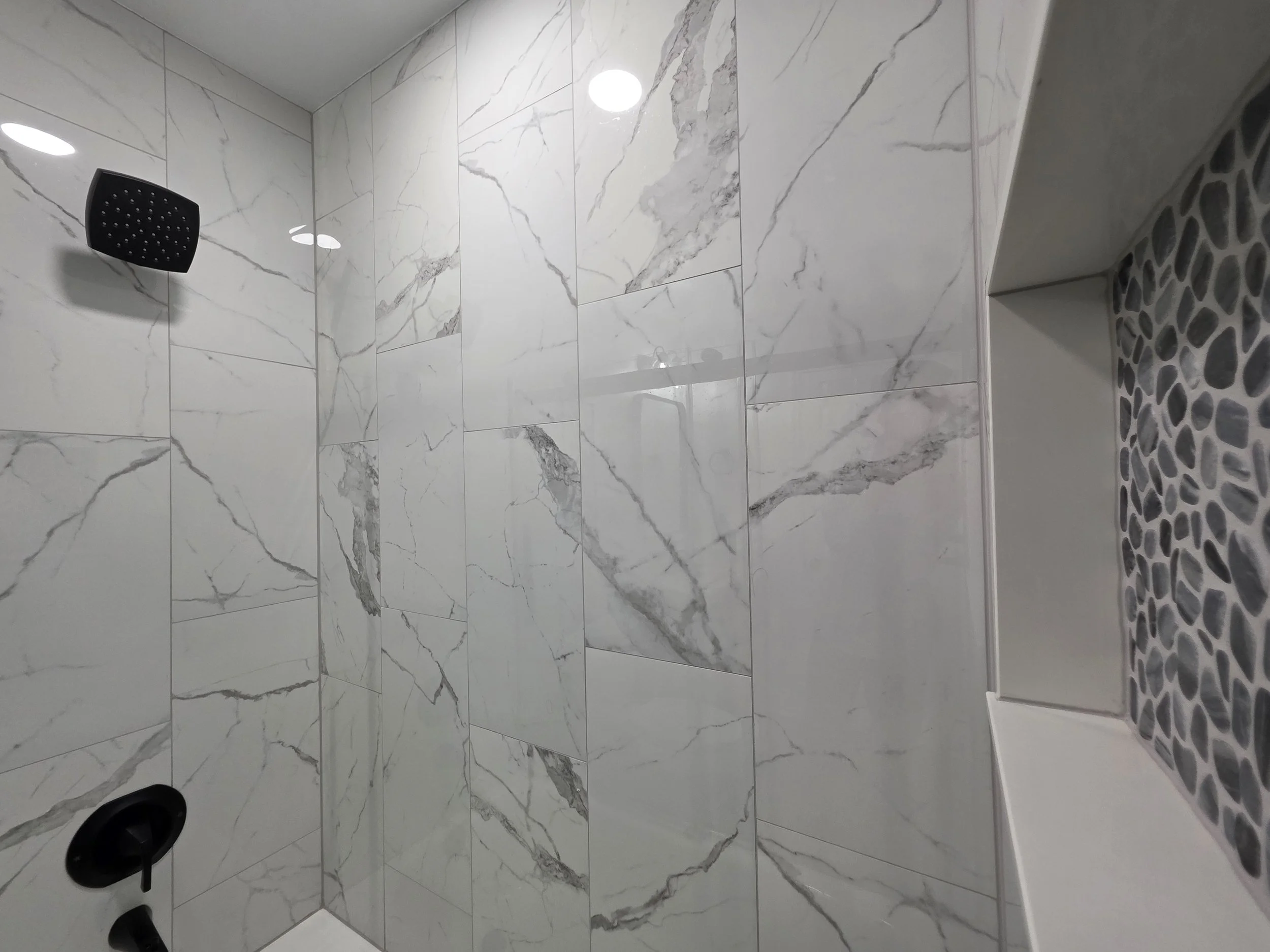 Upper tub surround showing the black showerhead and marble-look wall tile.