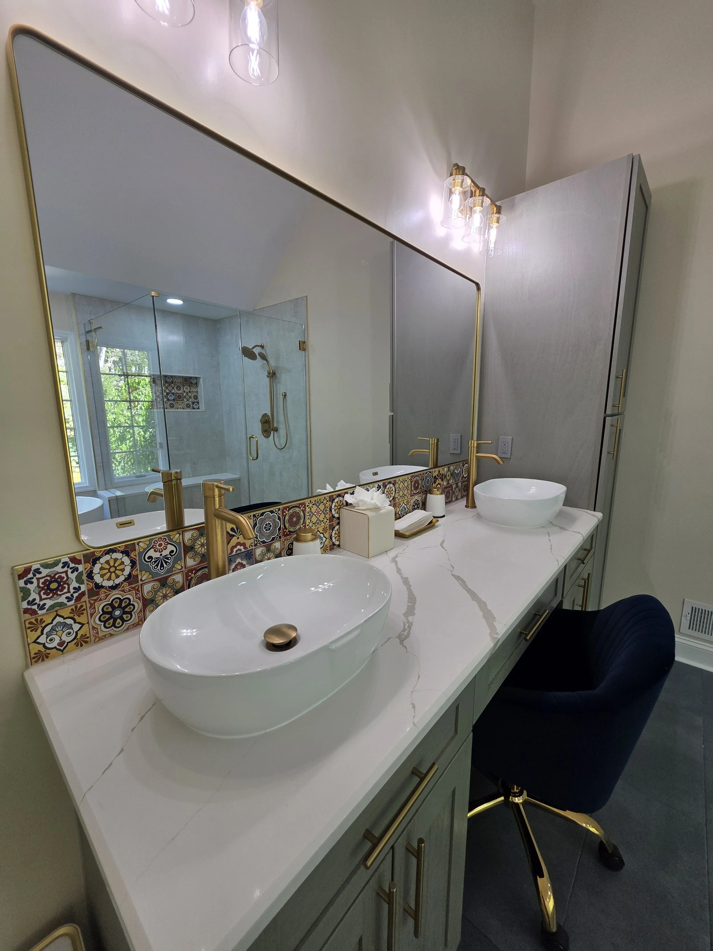 Close view of vessel sinks and gold-tone faucets against a patterned vanity backsplash.