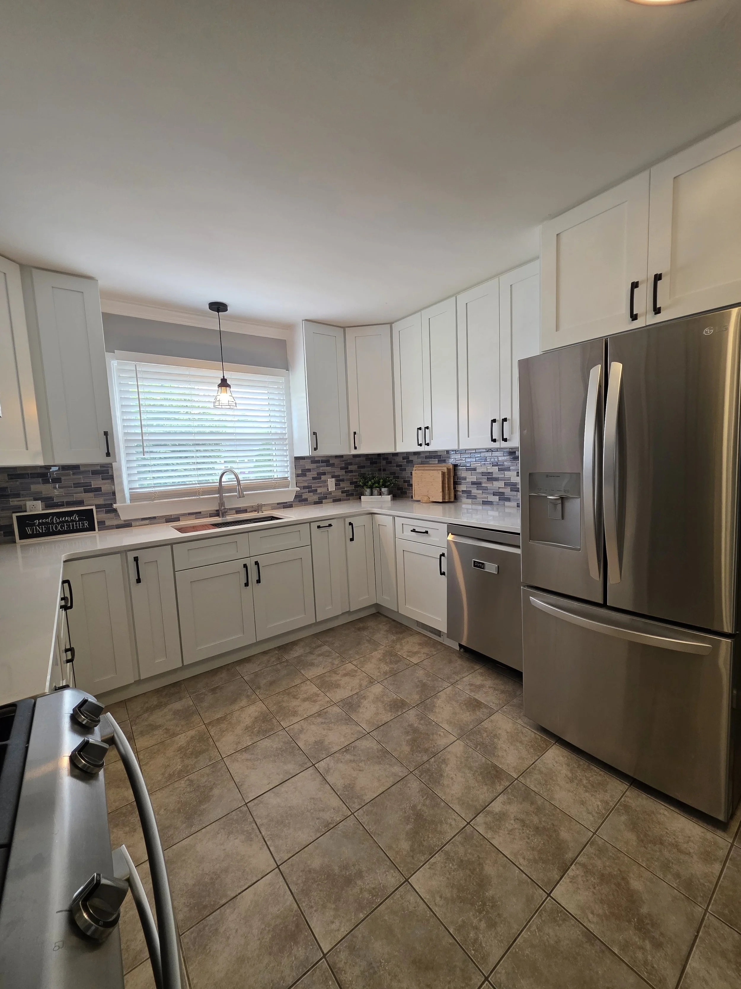 White kitchen cabinetry beside stainless refrigerator and window.