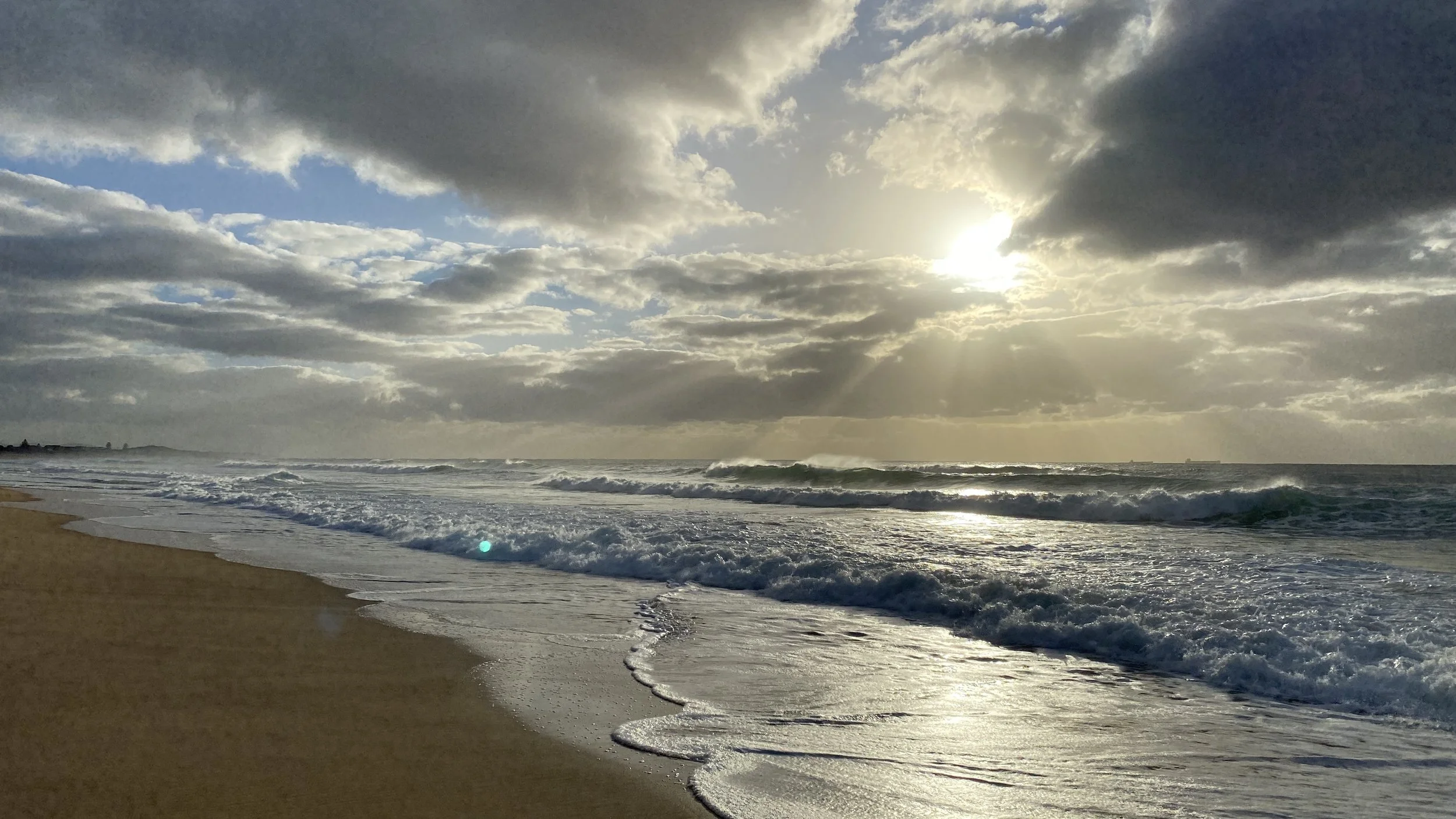 The surf and sky in the early morning on the NSW coast.  Water is swirling on the sand, and clouds fill the sky.