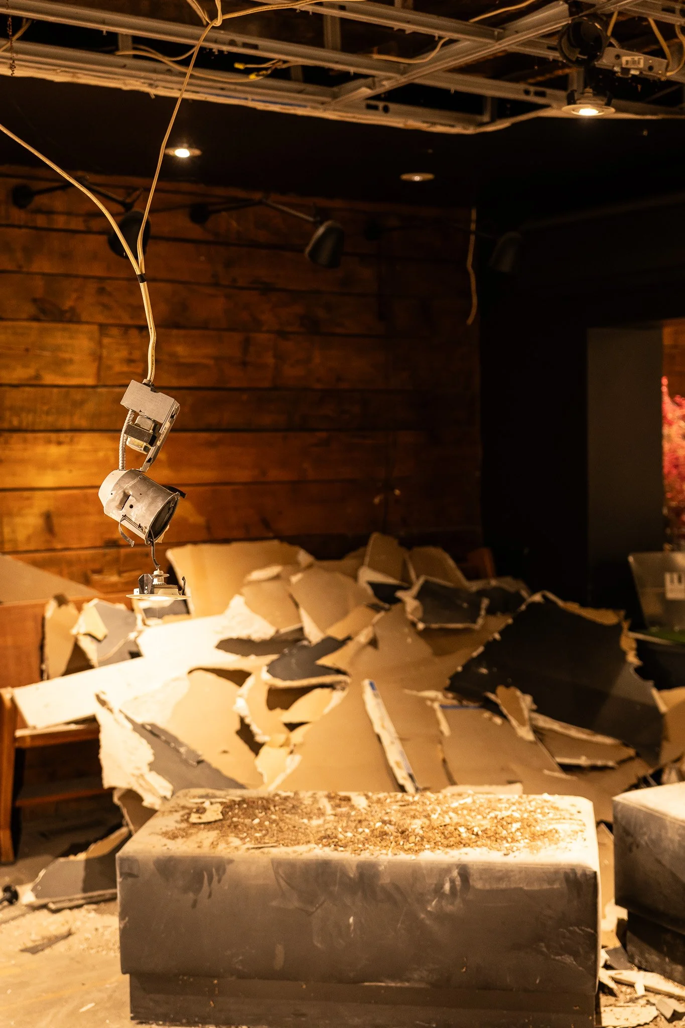 Un intérieur endommagé avec des débris au sol et des câbles électriques suspendus au plafond.