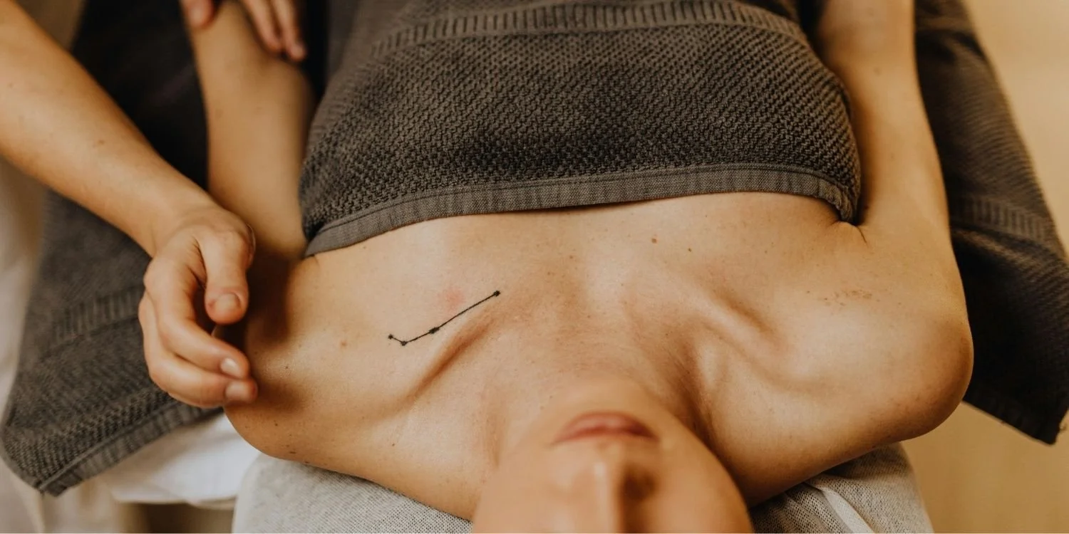 A person lying on their back with their shirt lifted, showing their bare chest with a small tattoo and visible chest and arm muscles.