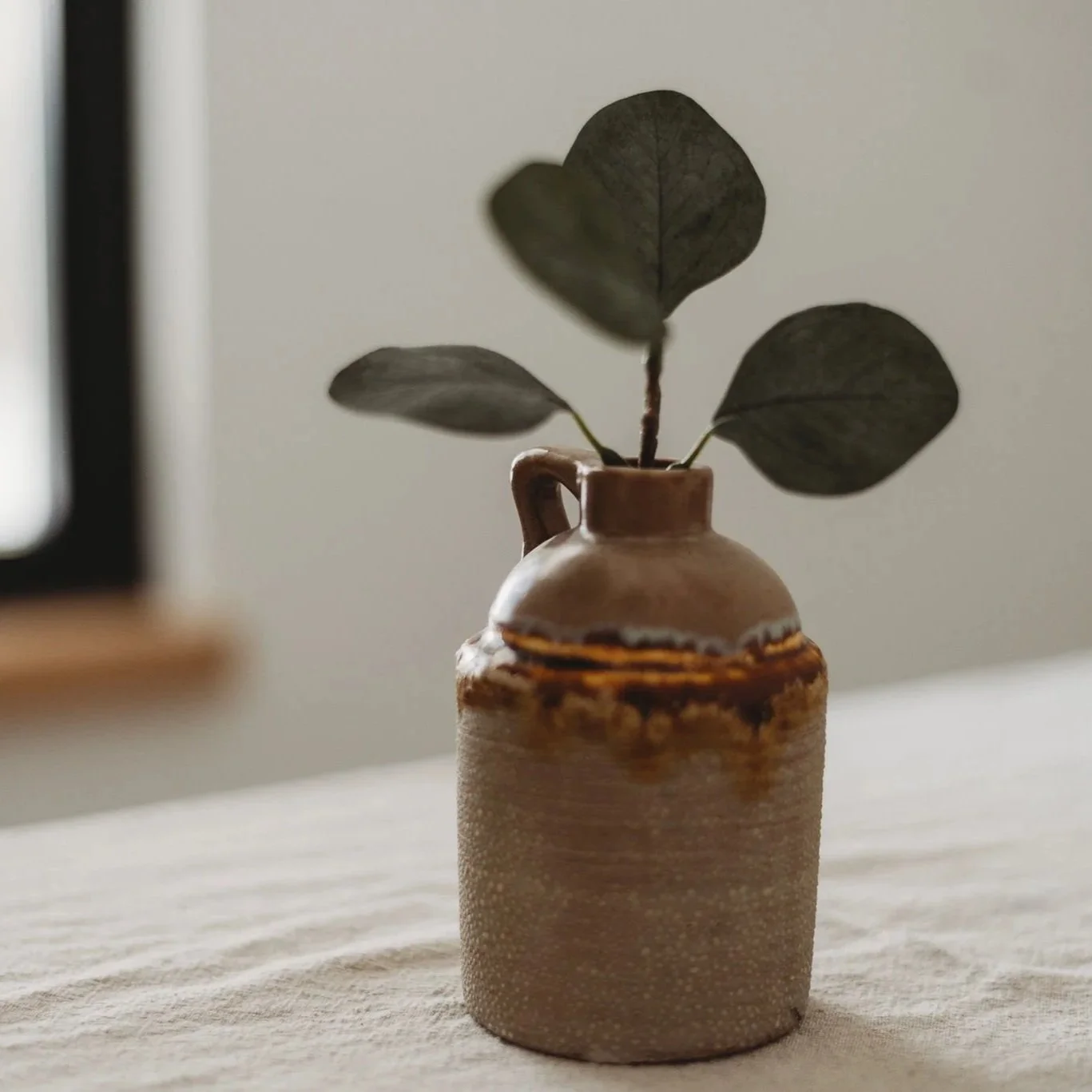 Ceramic vase with a rough texture and a brown glaze, holding four dark green leaves.