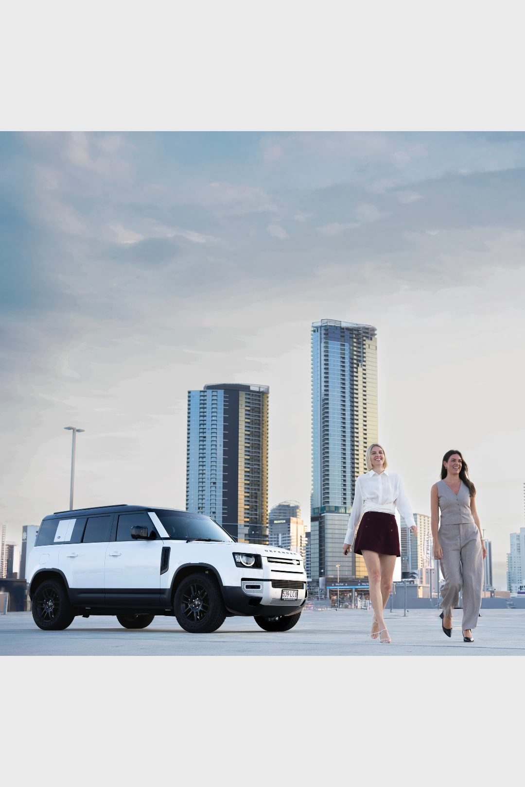 Two women walking through the Pacific Fair Shopping Centre car park beside a white Range Rover, photographed for an event promotion