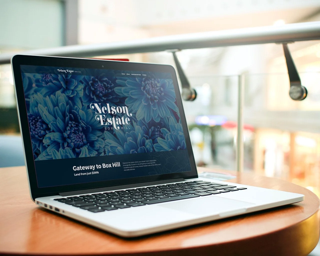 Laptop displaying a website for Nelson Estate in Box Hill, with floral background and pricing details.