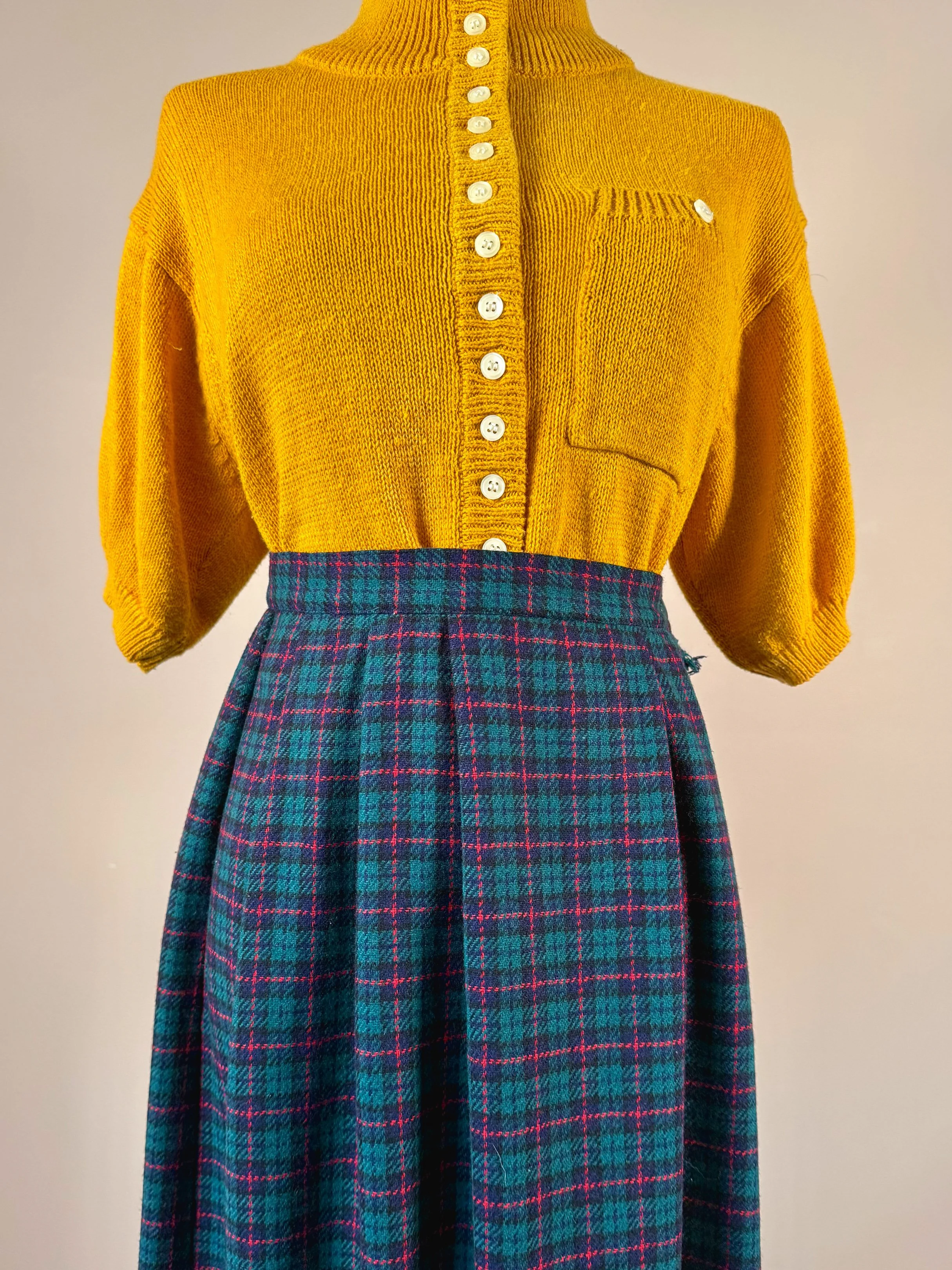 A mannequin wearing a yellow button-up sweater with three-quarter sleeves and a plaid skirt with green, red, and blue pattern.