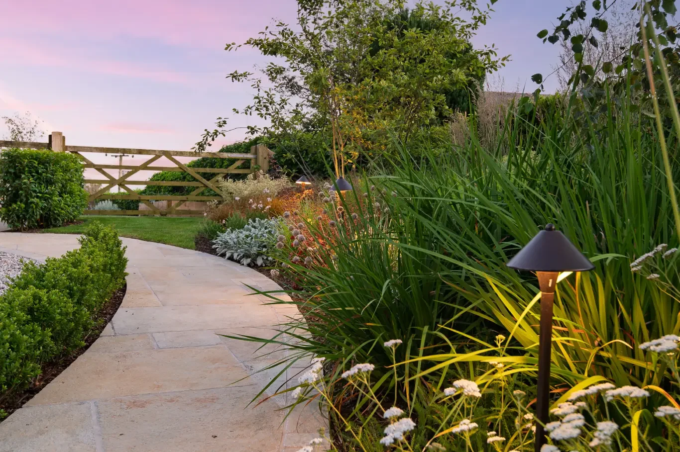 A backyard garden space featuring a wood and brick structure with a black outdoor fireplace or stove. The area is decorated with various potted plants and lush green foliage, creating a vibrant and cozy outdoor scene.