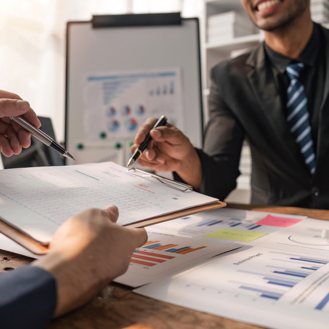 Two people reviewing and discussing financial documents and charts in an office.