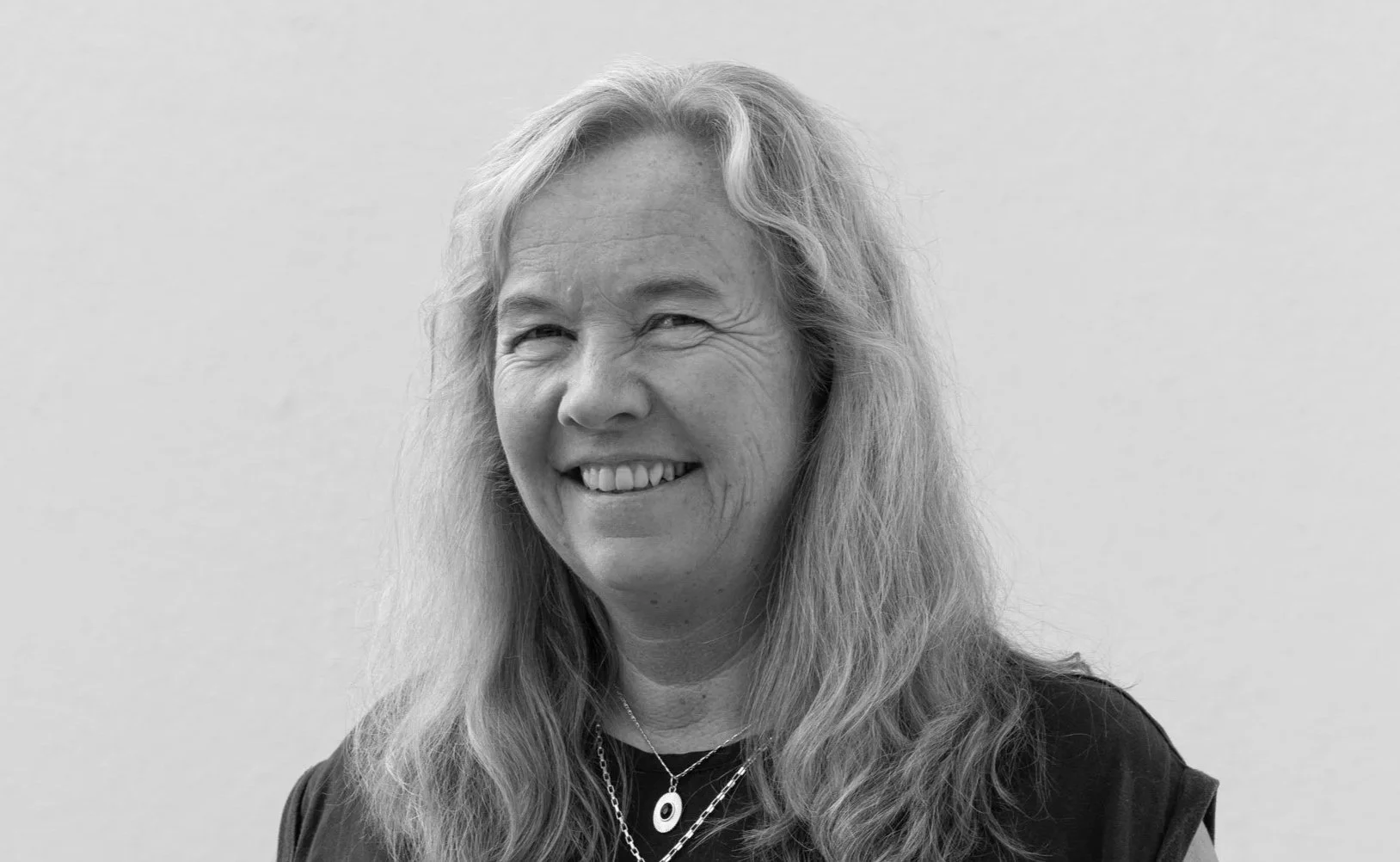 Portrett av en kvinne med brunt hår og briller, smilende, i svart-hvitt