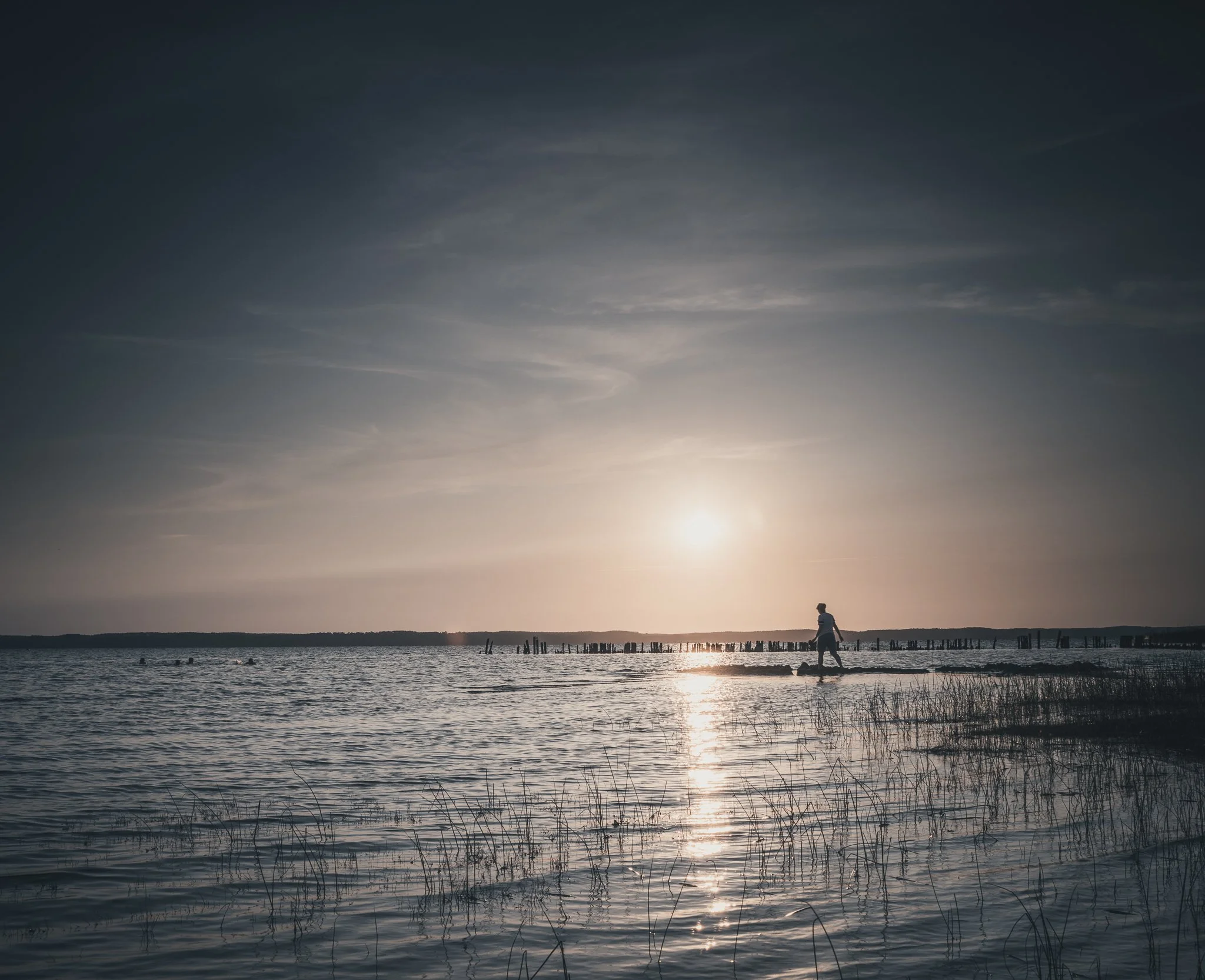 A person walking along the shoreline of a body of water during sunset with the sky partly cloudy.