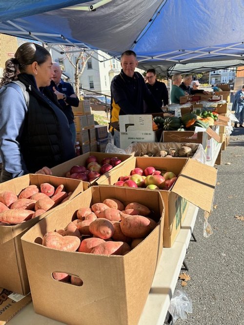 Local farmers market with volunteers and fresh produce under blue tents.