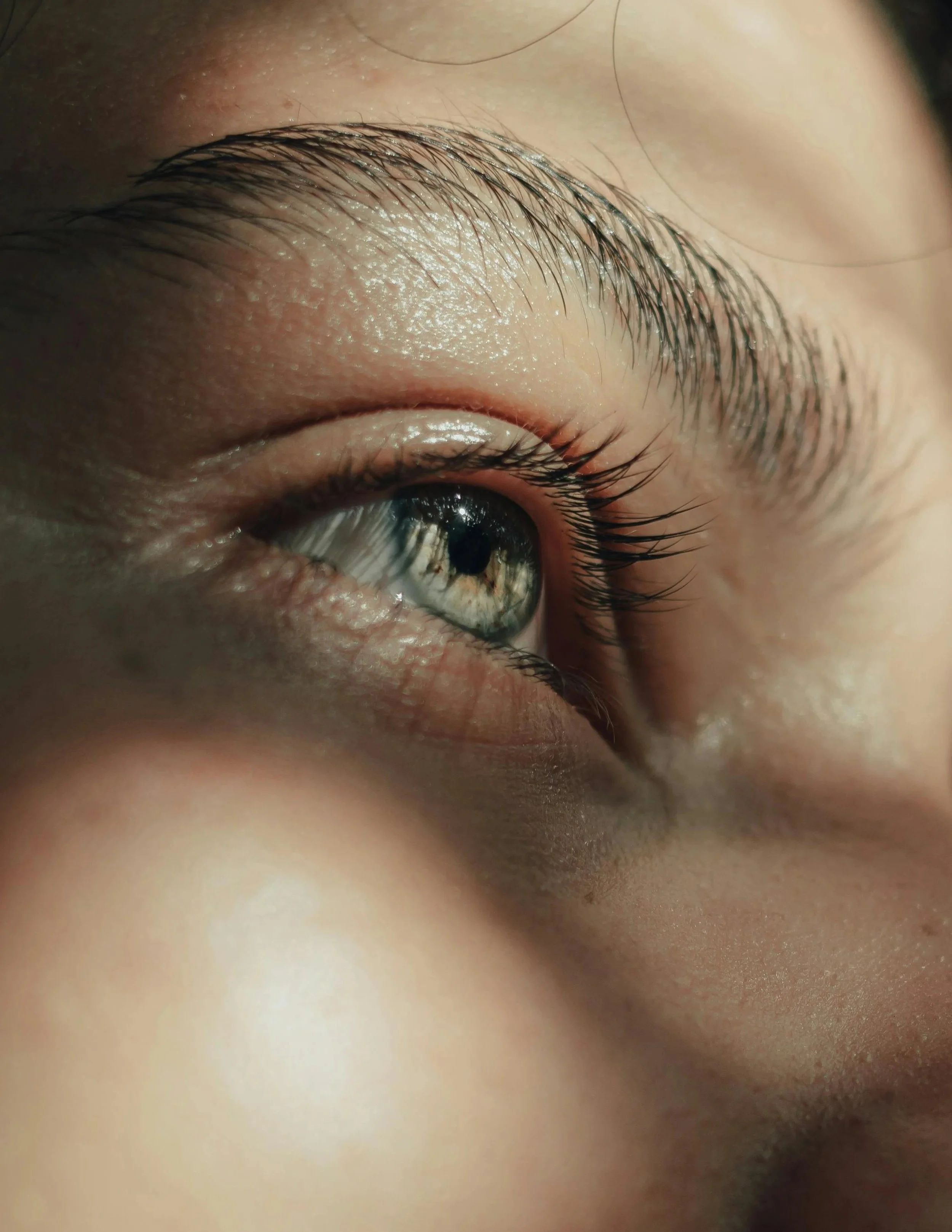 Close-up of a person's eye with green iris and long eyelashes, showing detailed skin texture and reflections in the eye.