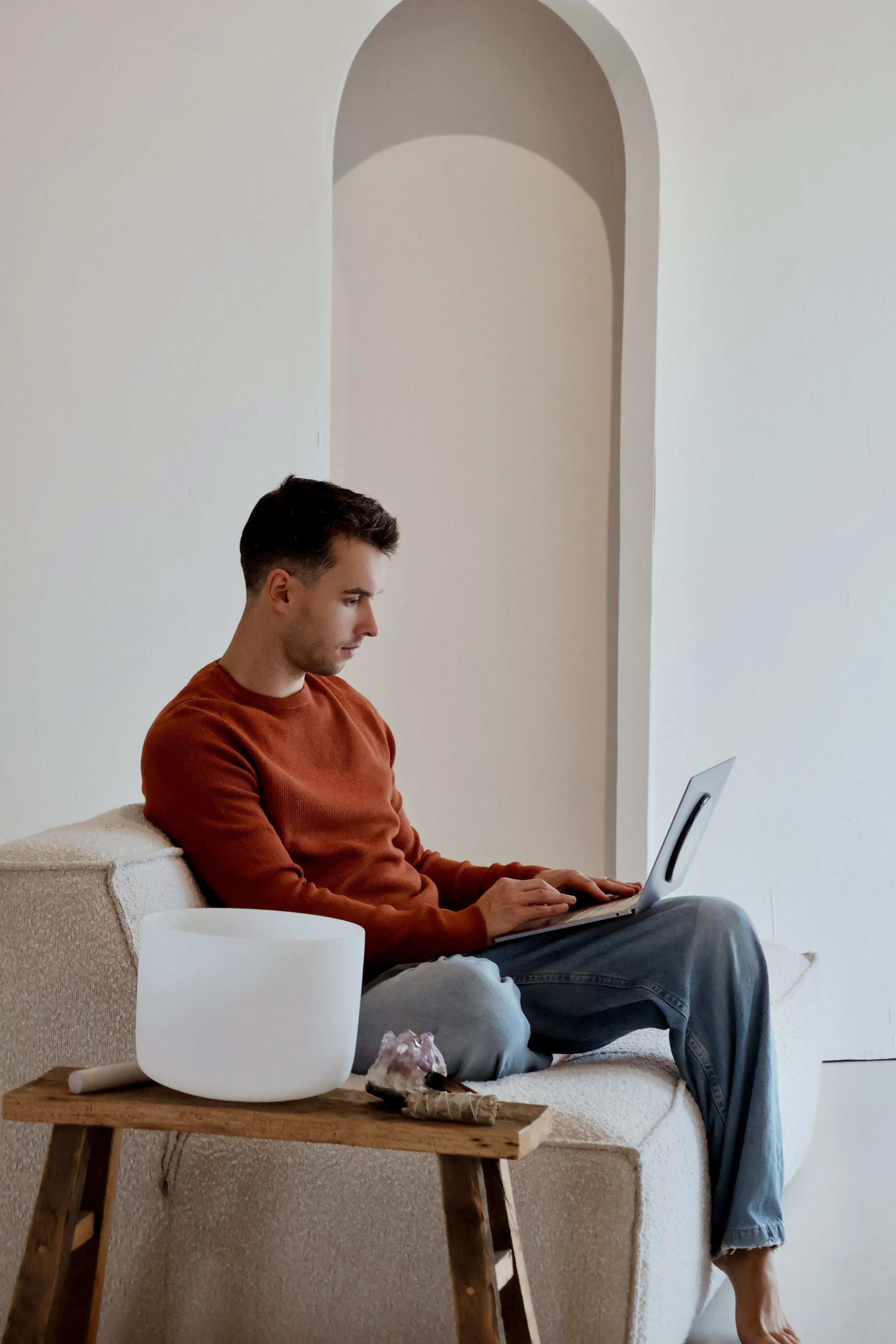 A young man sitting on a beige sofa, working on a laptop.