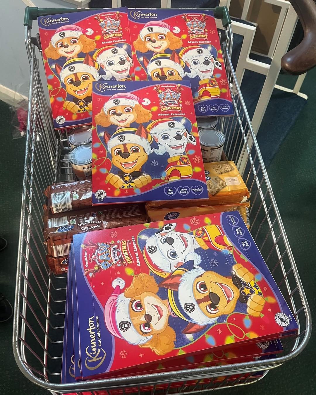 Shopping cart filled with Paw Patrol Christmas advent calendars, and some cans and chocolate bars.
