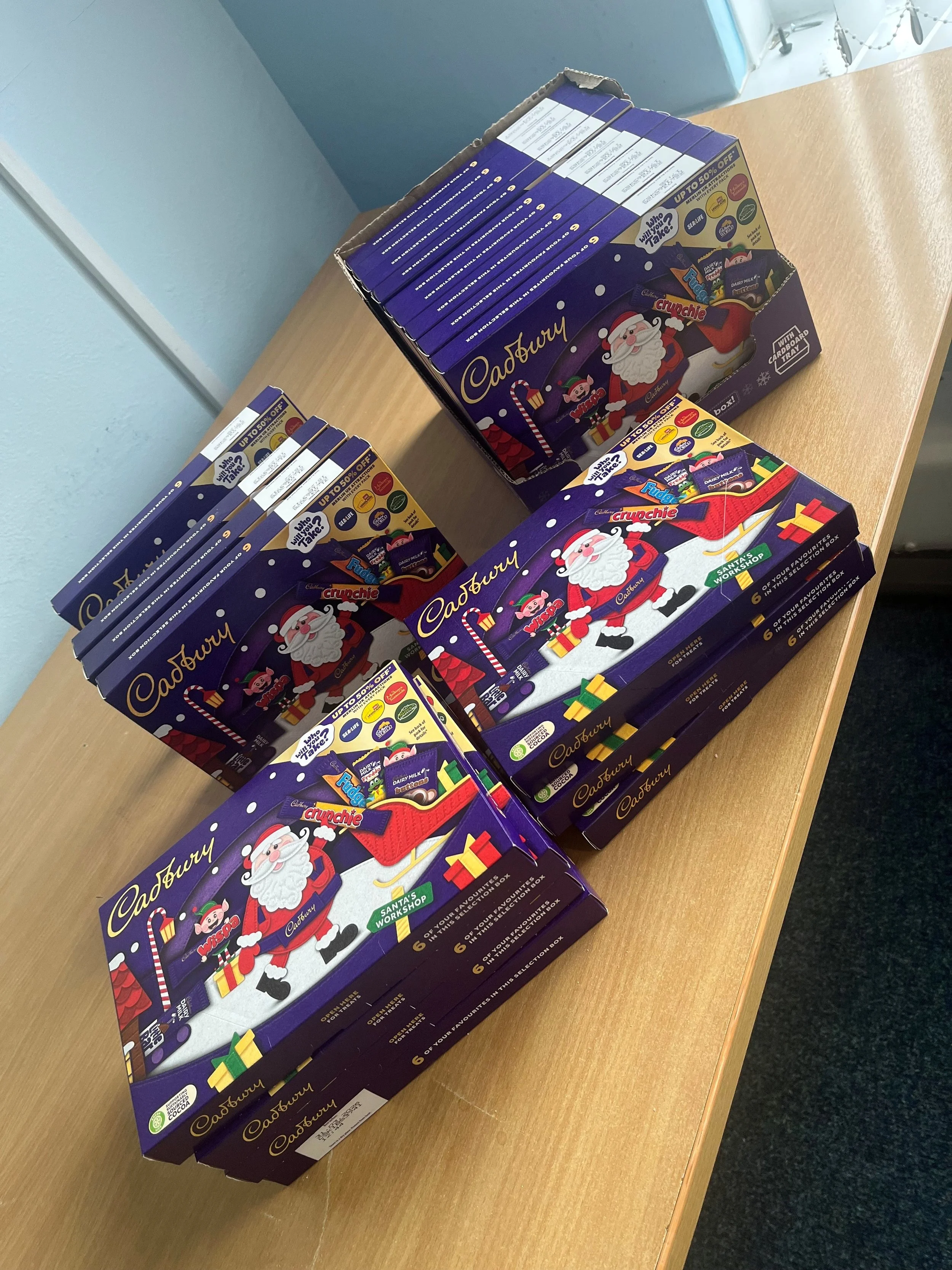 Three boxes of Cadbury Christmas chocolate with Santa Claus and Christmas-themed packaging on a wooden table.