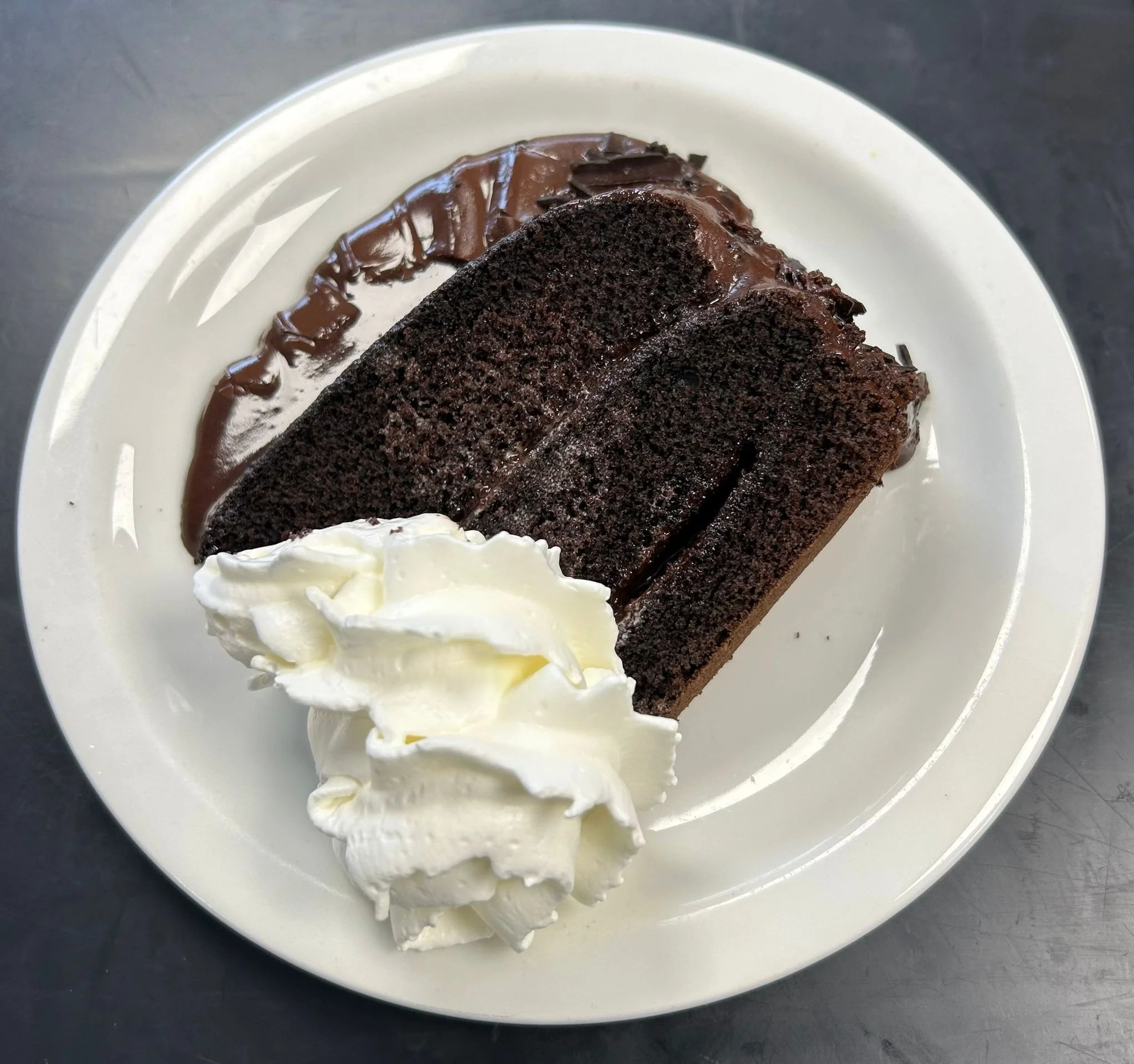 A white plate with two slices of chocolate cake topped with chocolate frosting, a swipe of chocolate frosting on the side of the plate, and a dollop of whipped cream.
