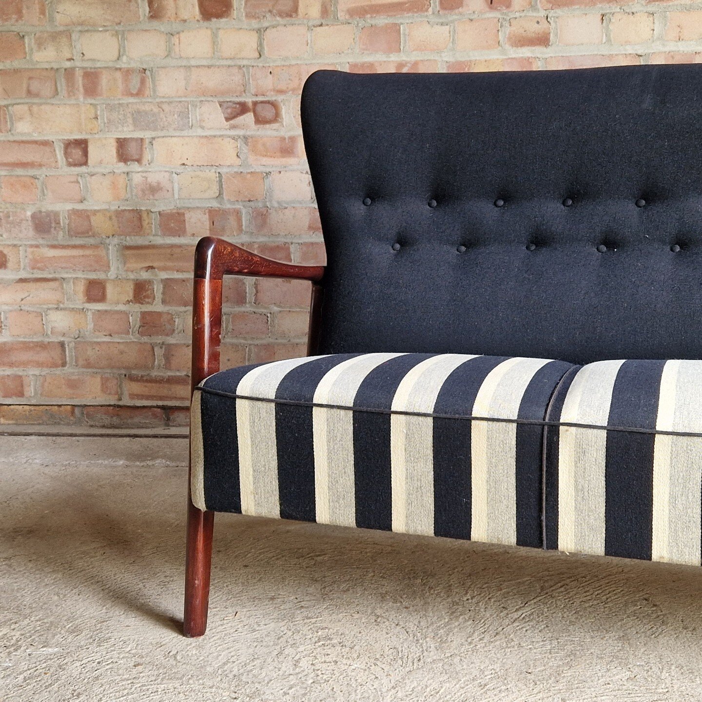 A 1940s high-back sofa by Fritz Hansen, showcasing exposed wooden arms. The seat and back feature button detailing for added elegance.

This exquisite piece features a striking interplay of navy blue and white line wool on its seat, creating a captiv
