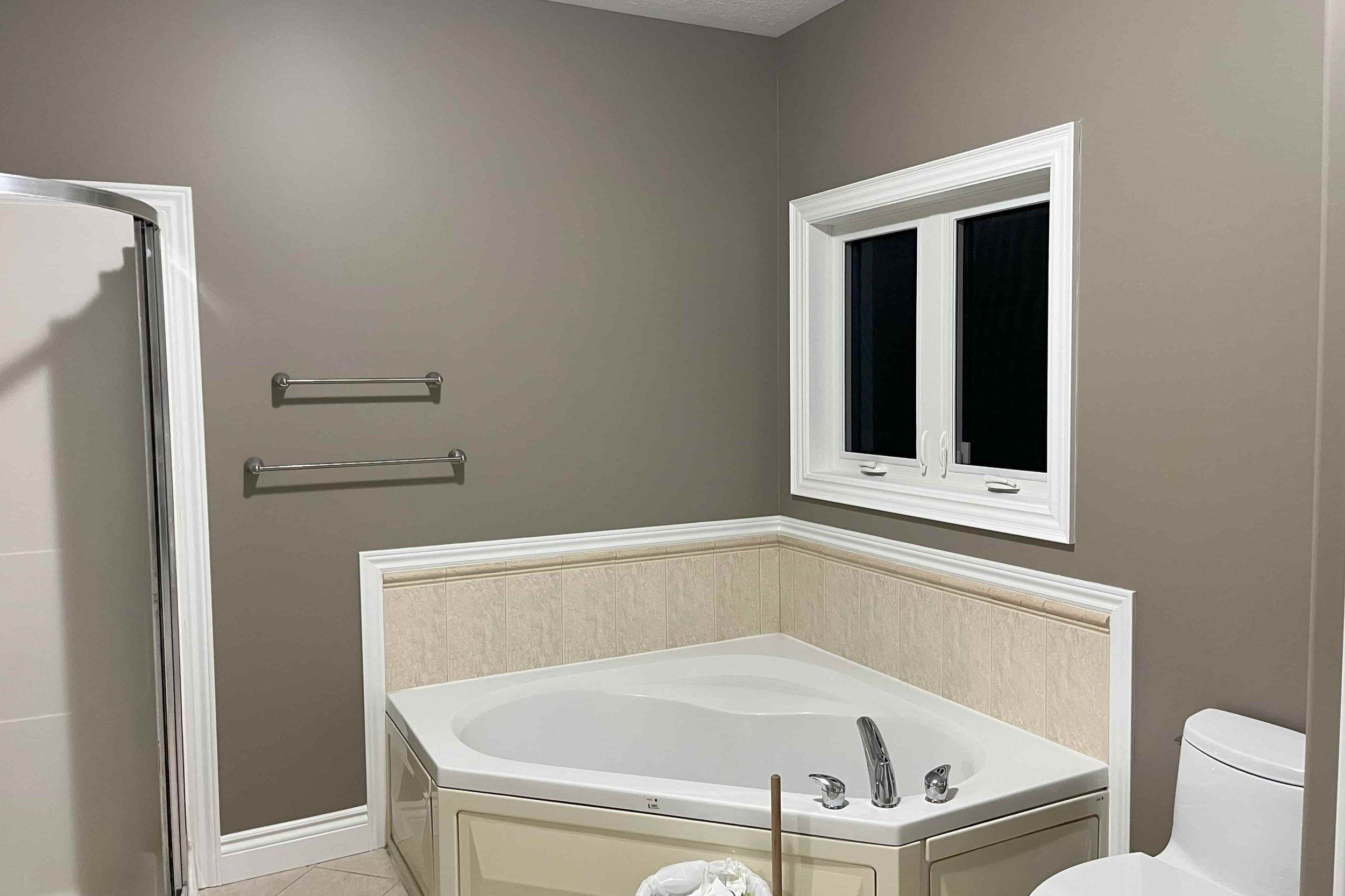 Bathroom with corner bathtub, shower stall, towel racks, window, and toilet.