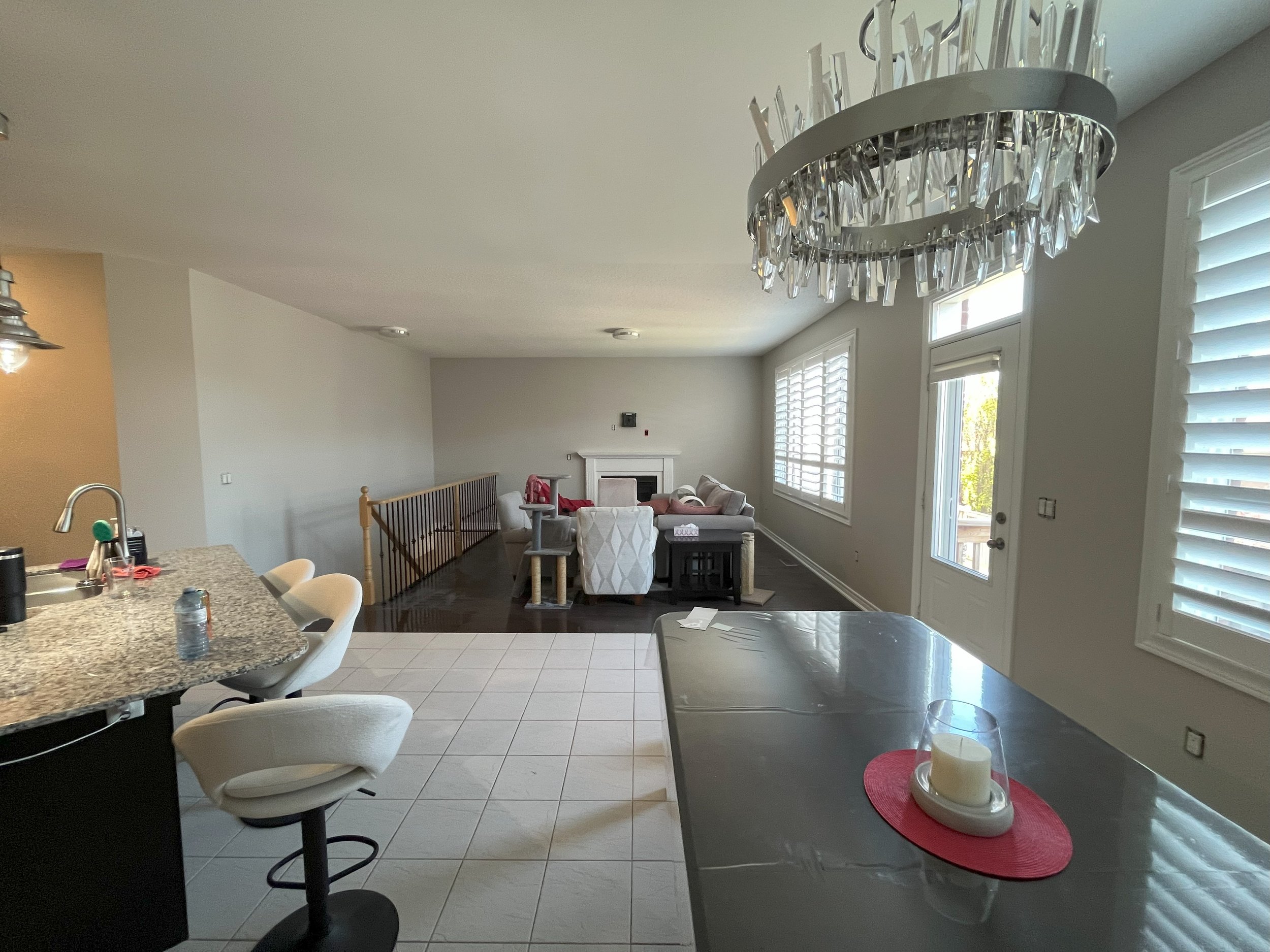 Open-concept living room and kitchen area with a chandelier, white walls, large windows, and a fireplace in the distance. Painted by expert painters in Durham Region.