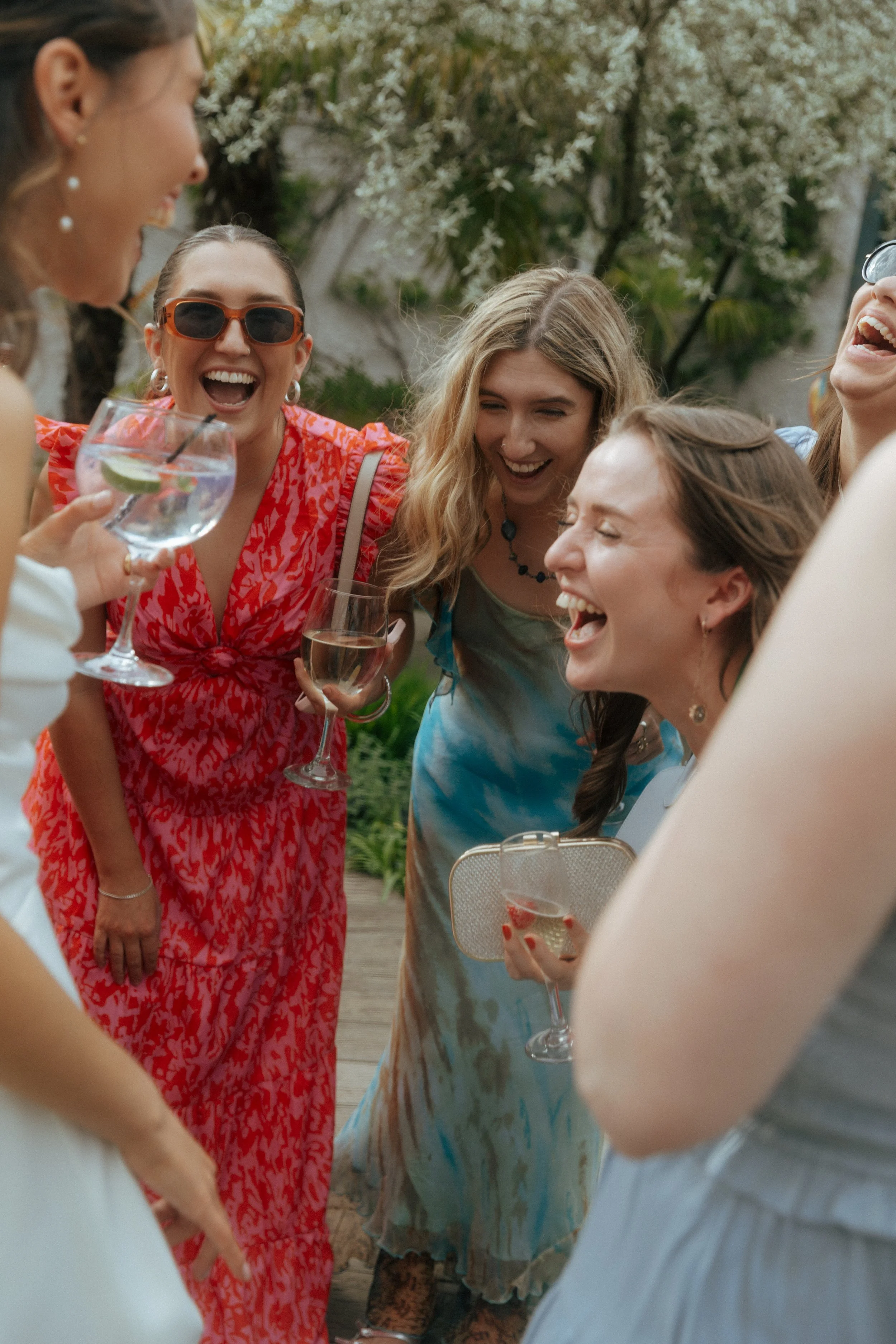 Group of women enjoying a celebration outdoors, holding drinks and laughing.