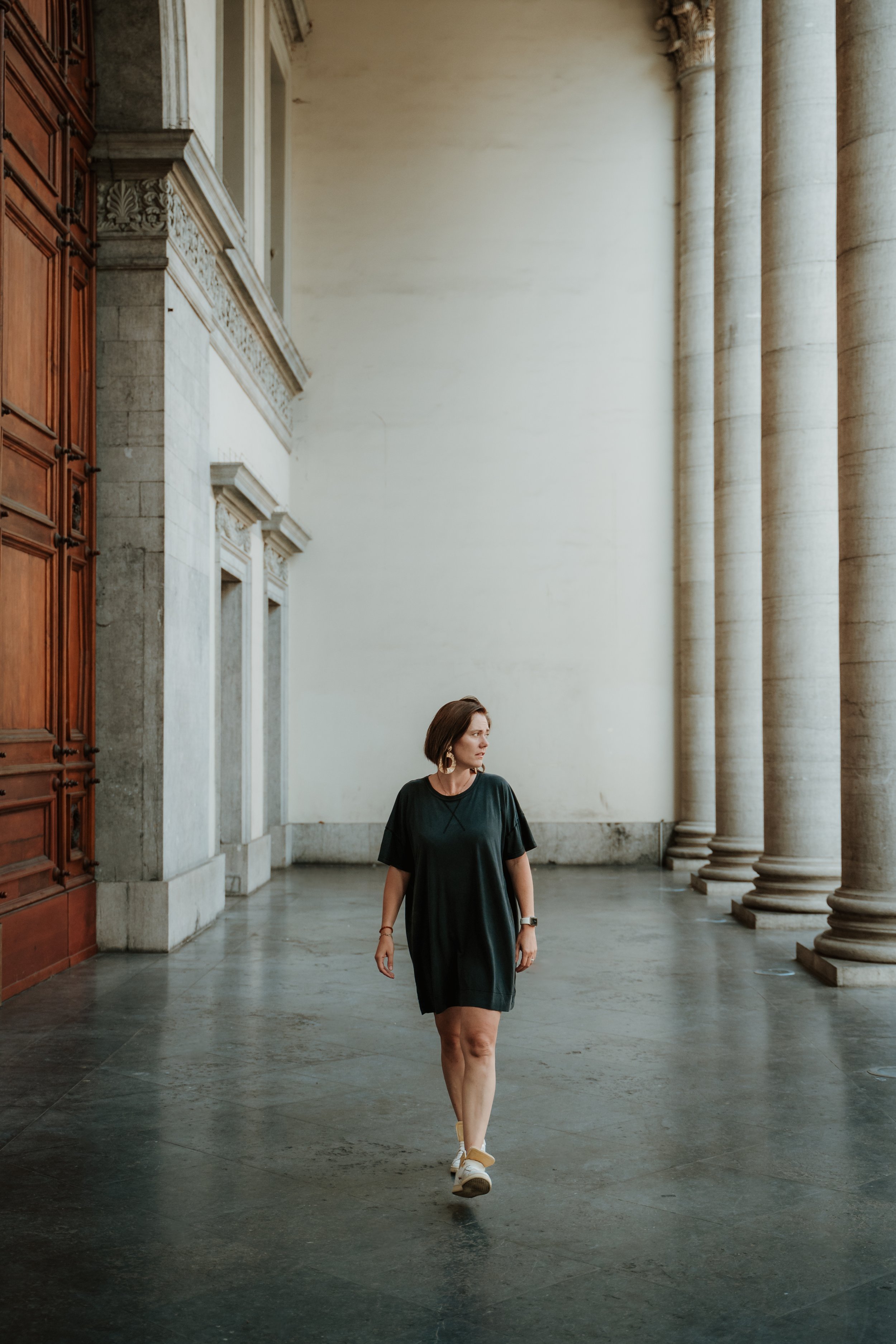 A woman in a black dress walking through a grand historic building with tall columns and ornate architecture.