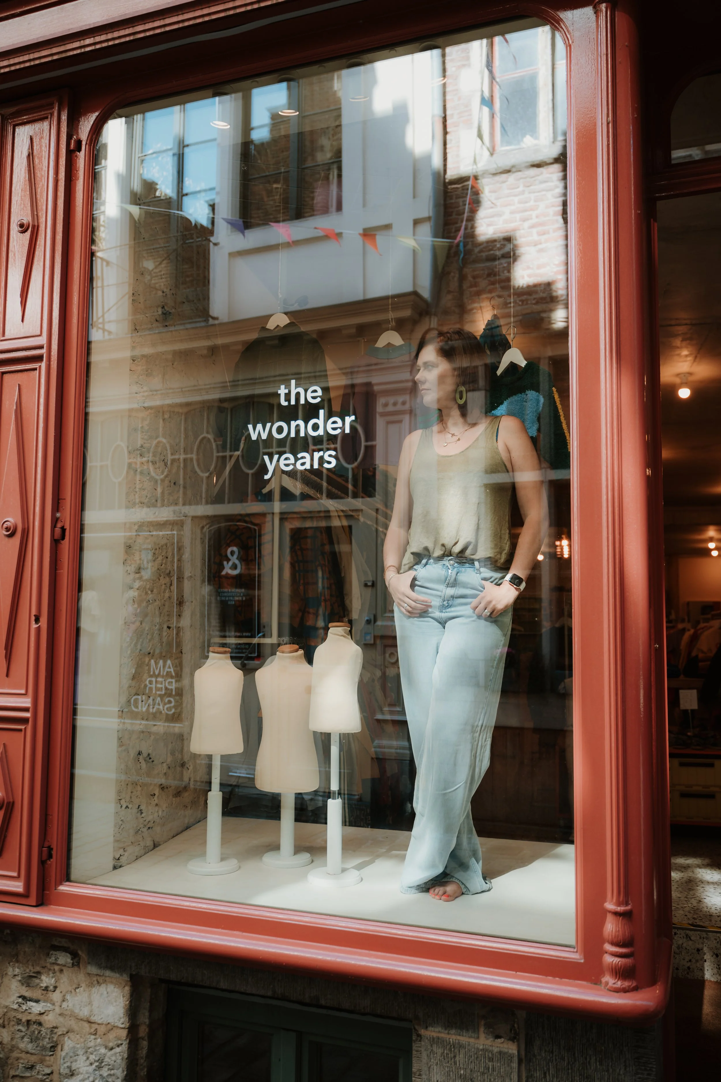 Store window display with a mannequin dressed in a sleeveless top and light-colored wide-leg pants. The window features the store name "the wonder years" and showcases several mannequin busts and clothing hangers inside.