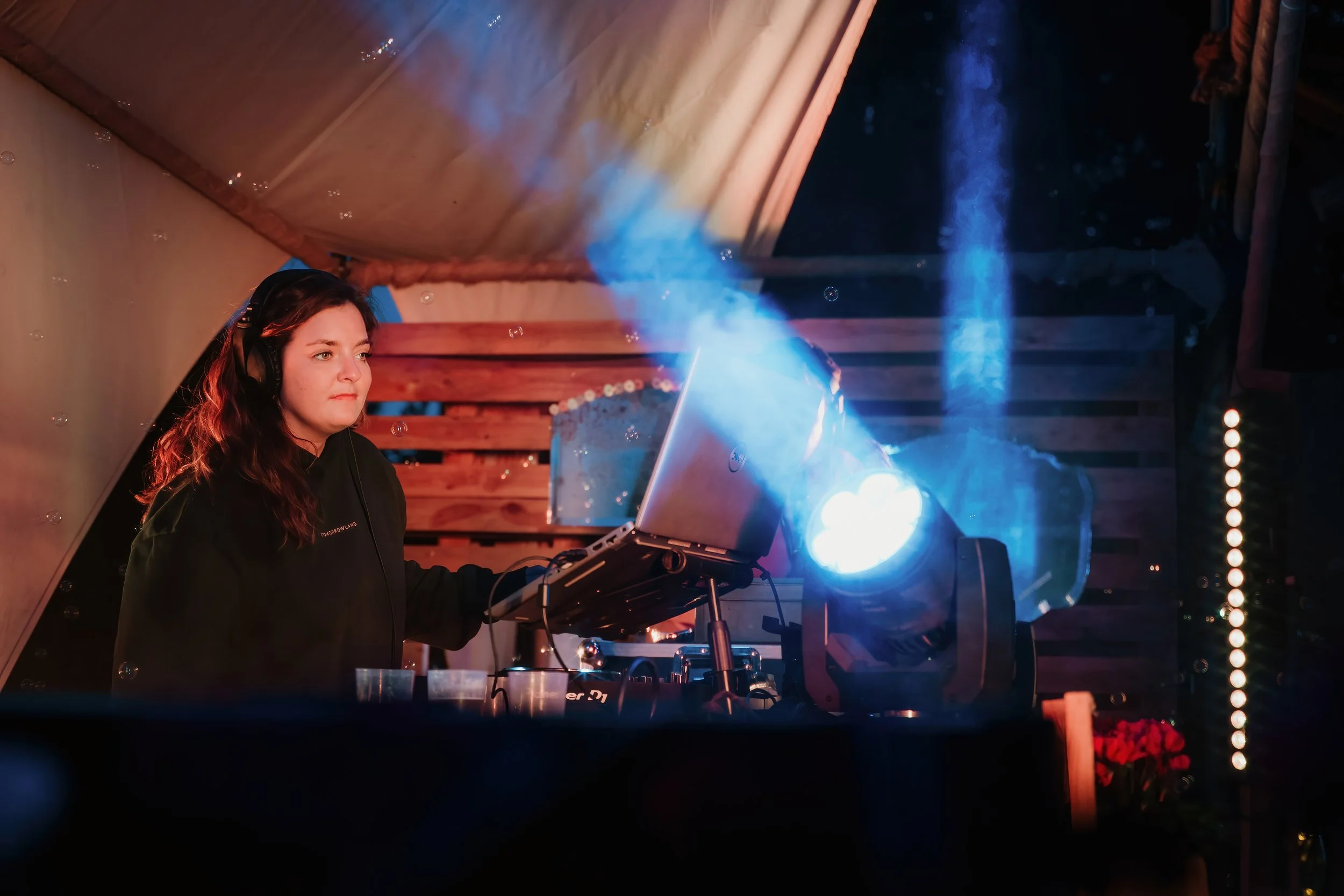 A woman wearing headphones operating DJ equipment at an outdoor event during the evening.