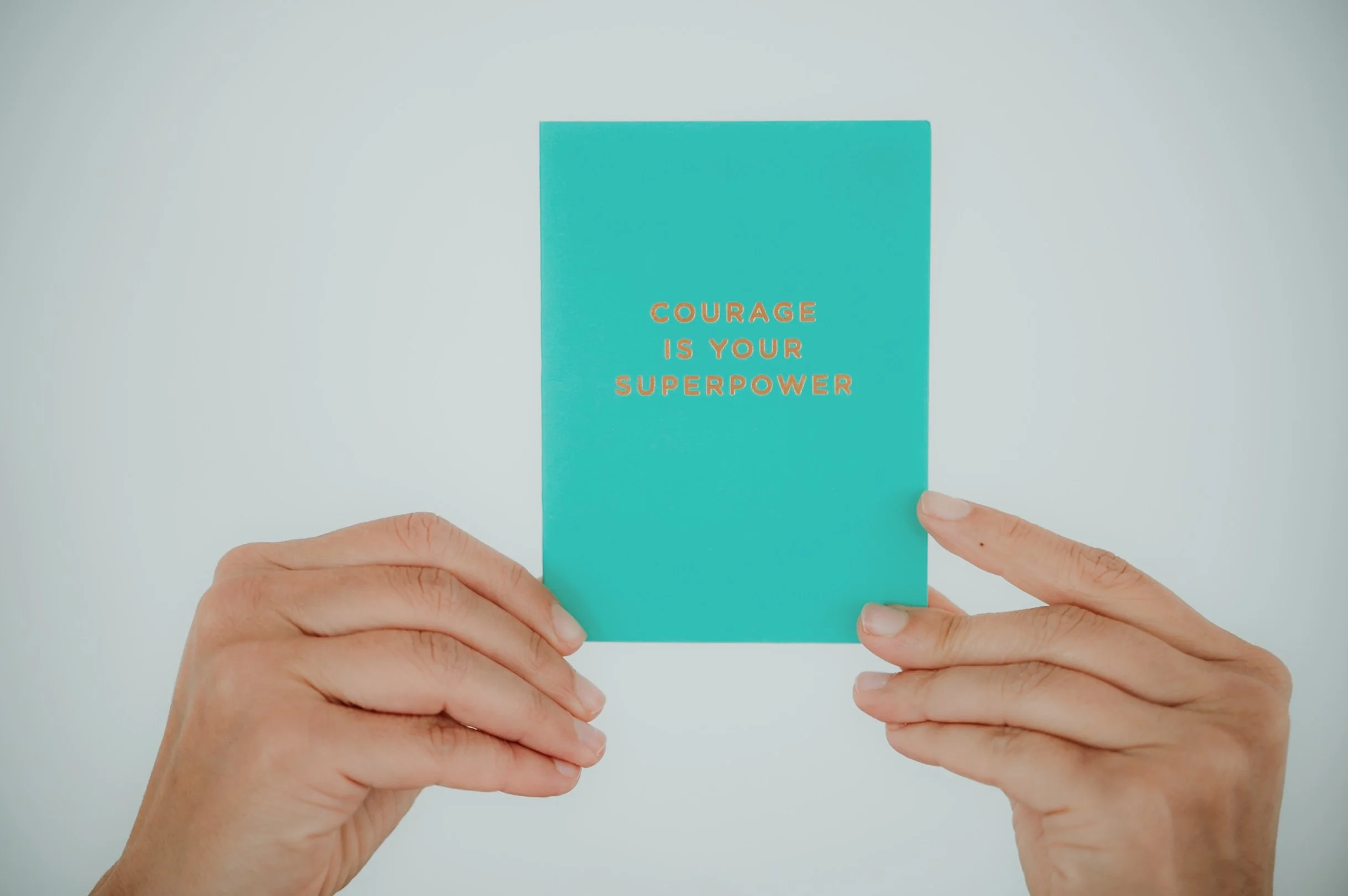 Close-up of hands holding a teal-colored card with orange text that reads, "Courage is your superpower."