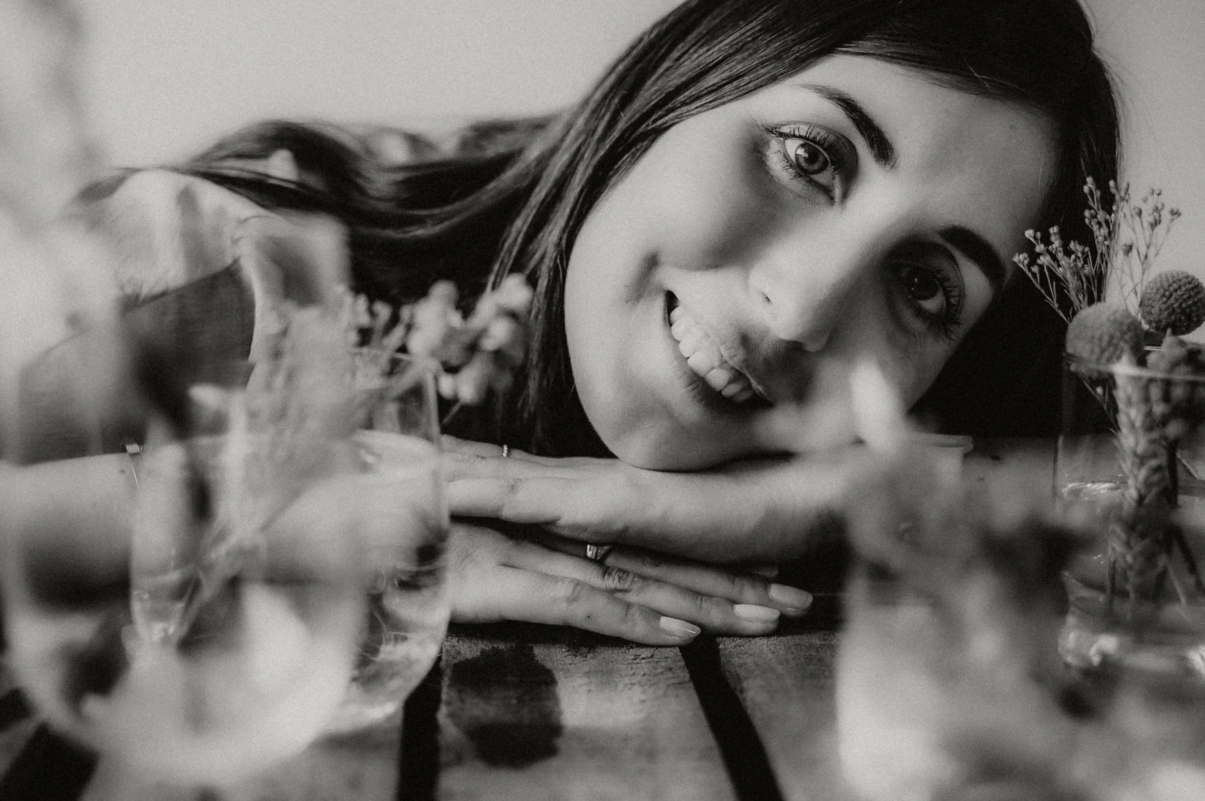 Black and white photo of a woman's face with her chin resting on her hands, surrounded by flowers and plants.